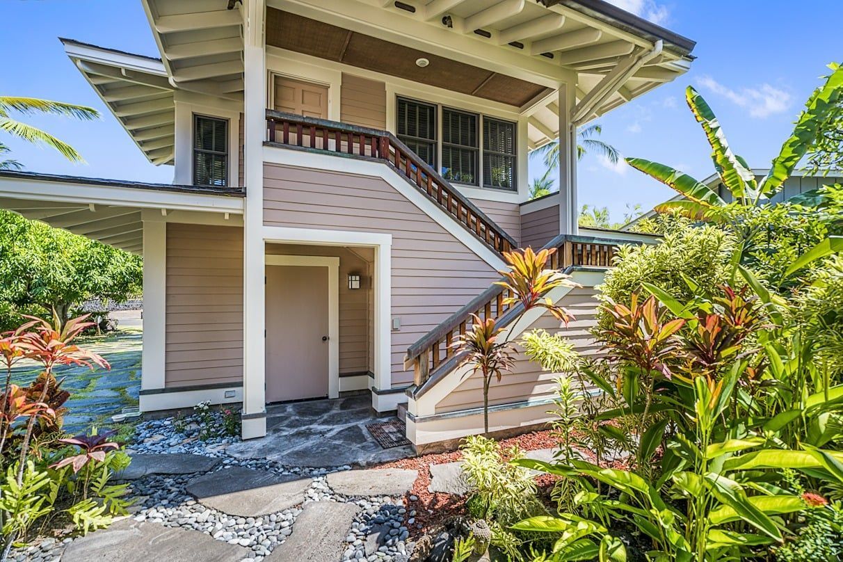 A house with stairs leading up to it is surrounded by trees and bushes.