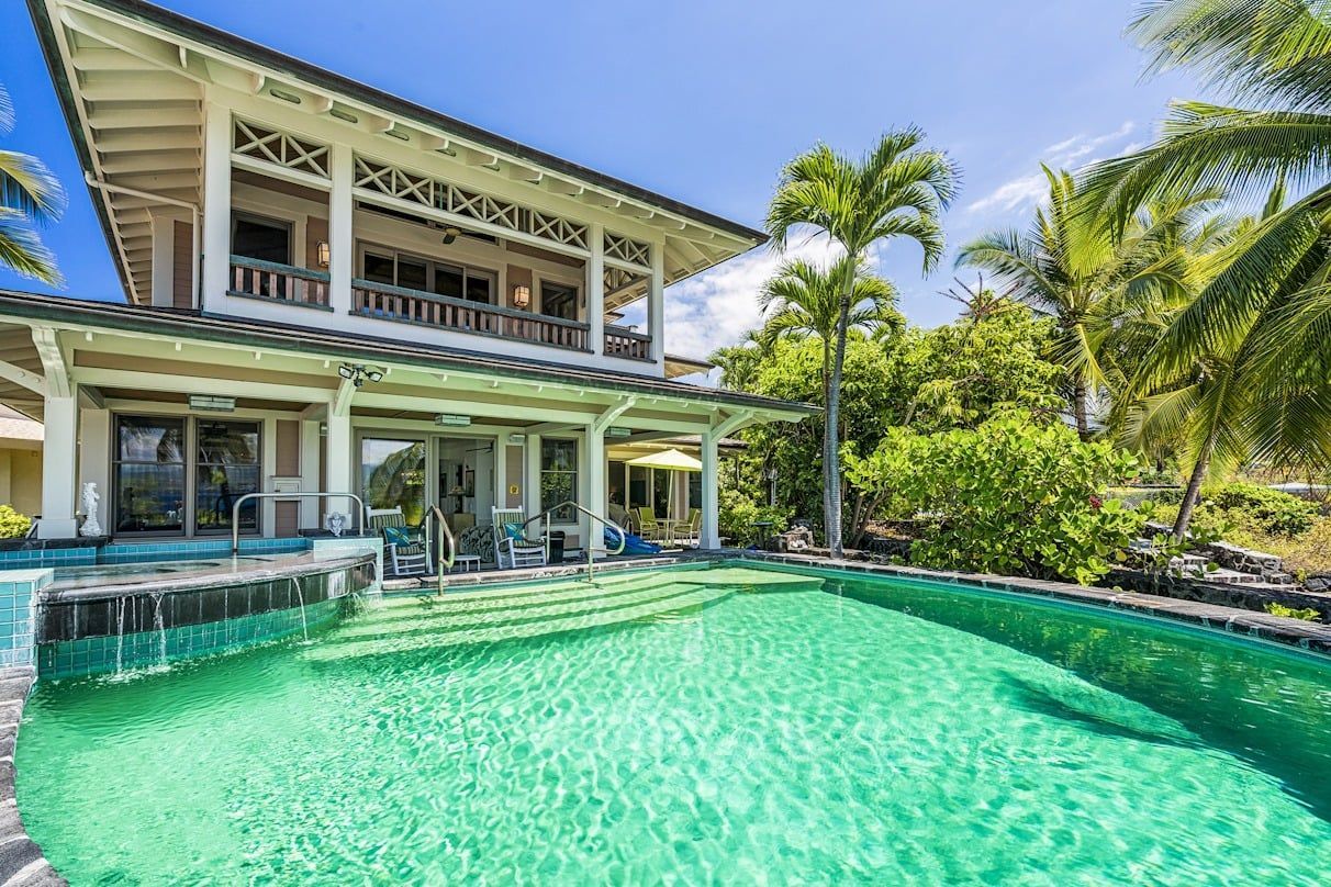 A large house with a swimming pool in front of it surrounded by palm trees.