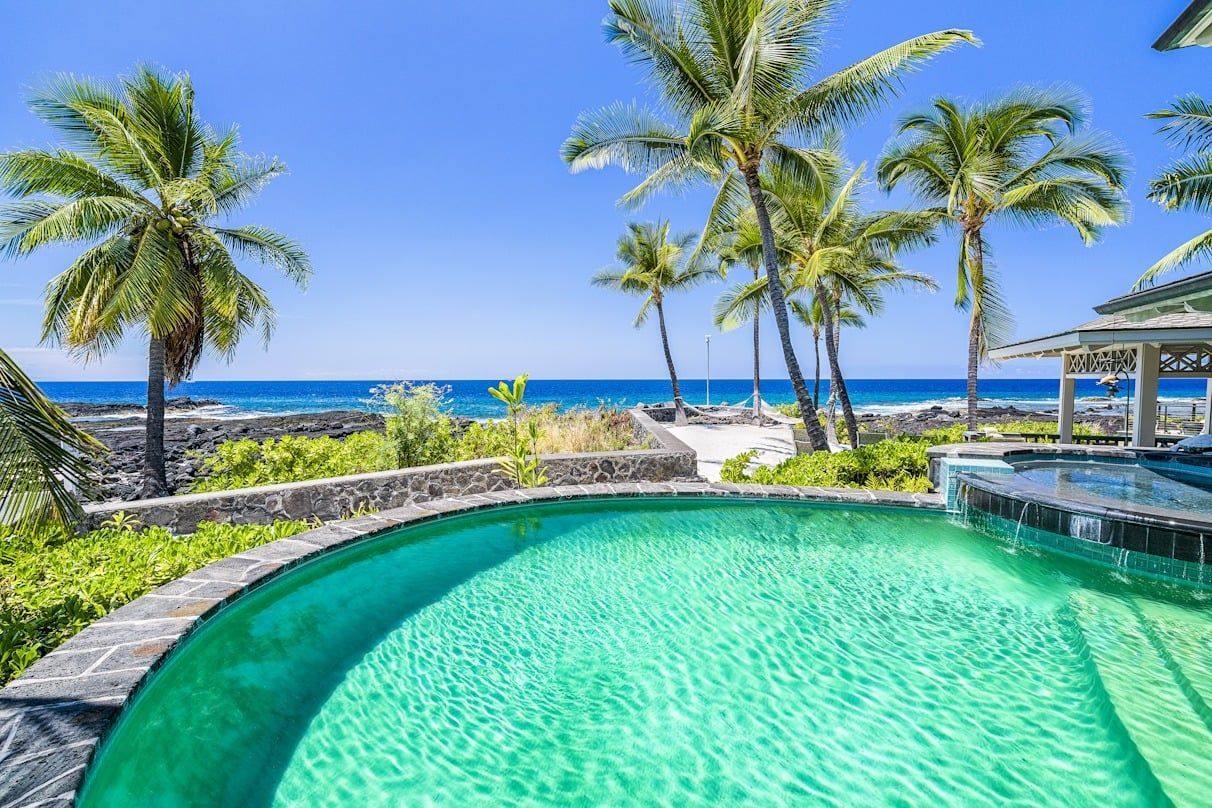 A large swimming pool with a view of the ocean and palm trees.