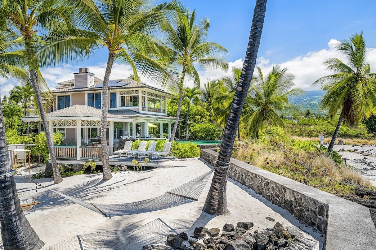 A large house is surrounded by palm trees on a tropical island.