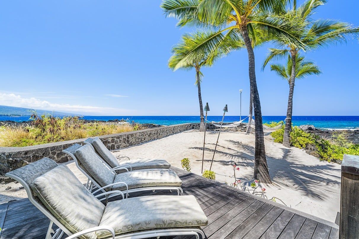 A row of lounge chairs on a wooden deck overlooking the ocean.