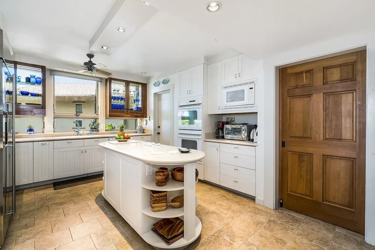 A kitchen with white cabinets , stainless steel appliances , a large island and a wooden door.