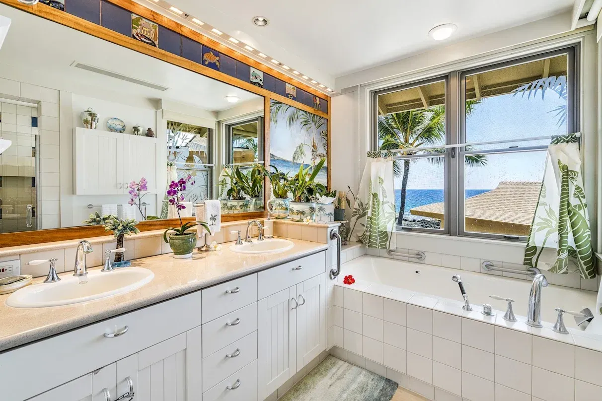 A bathroom with two sinks and a tub with a view of the ocean.