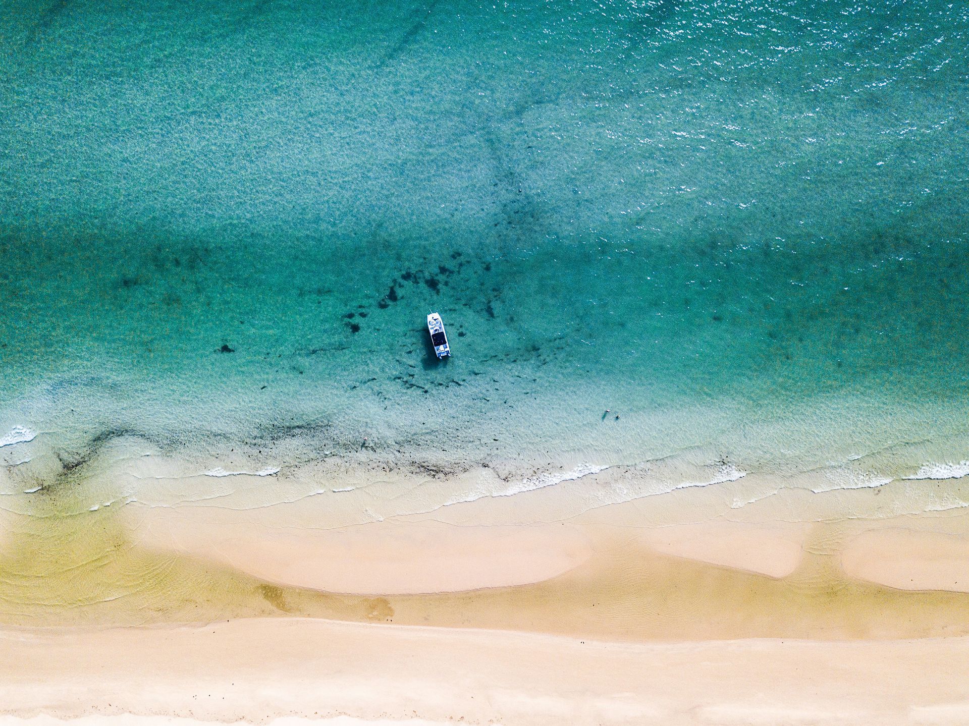An aerial view of a beach with a boat in the water.