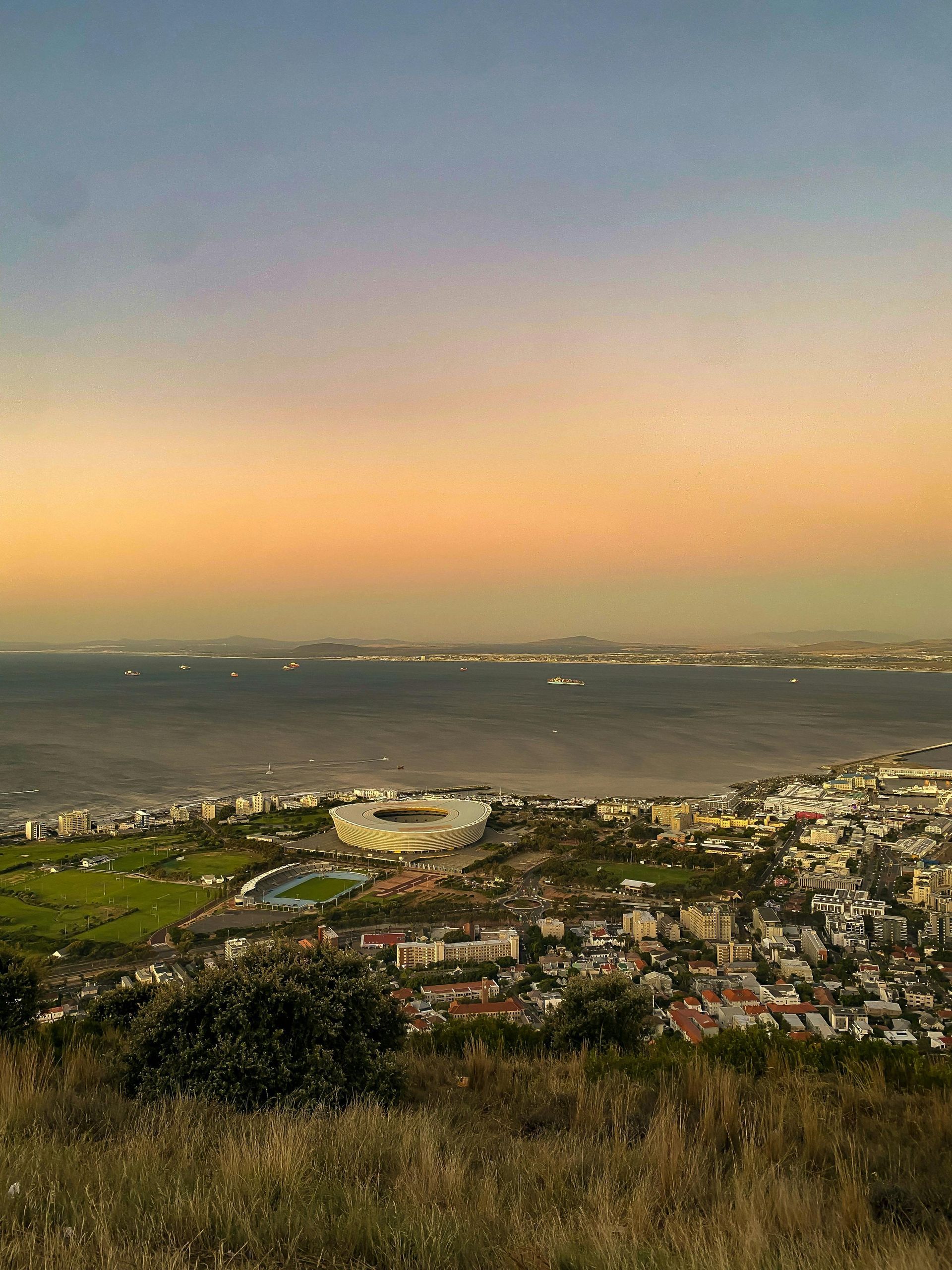 Coastal cityscape with a stadium by the ocean, under a colorful sunset sky.