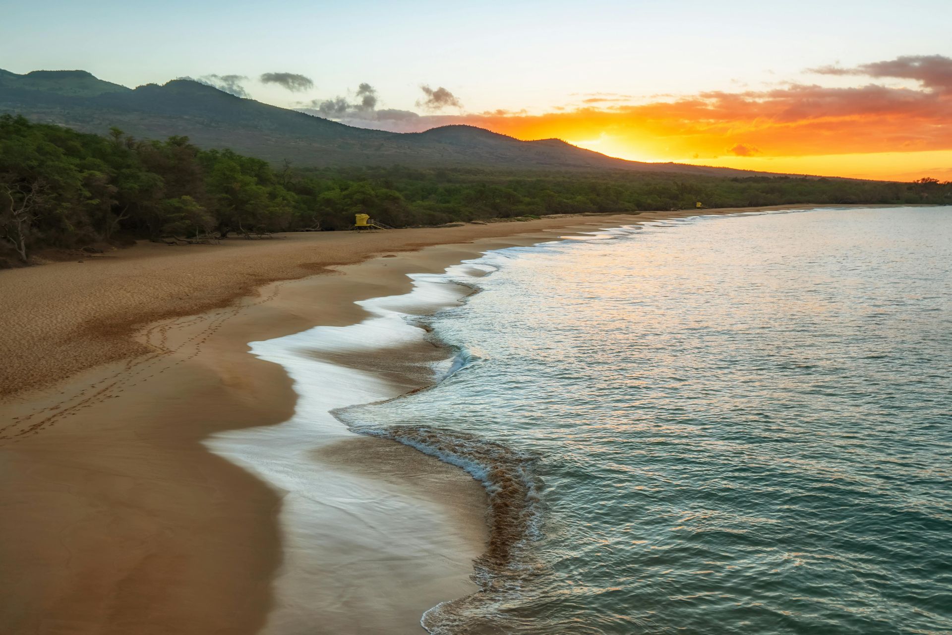 An aerial view of a beach at sunset with mountains in the background.