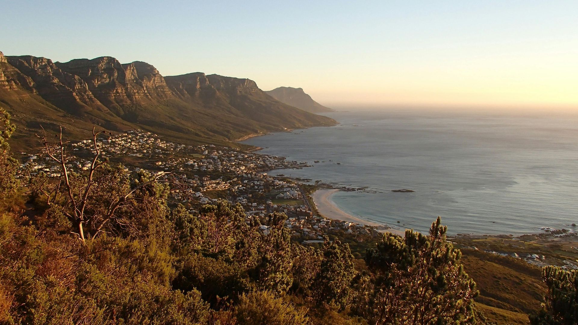 Coastal view with mountains, town, and ocean under a warm sky.