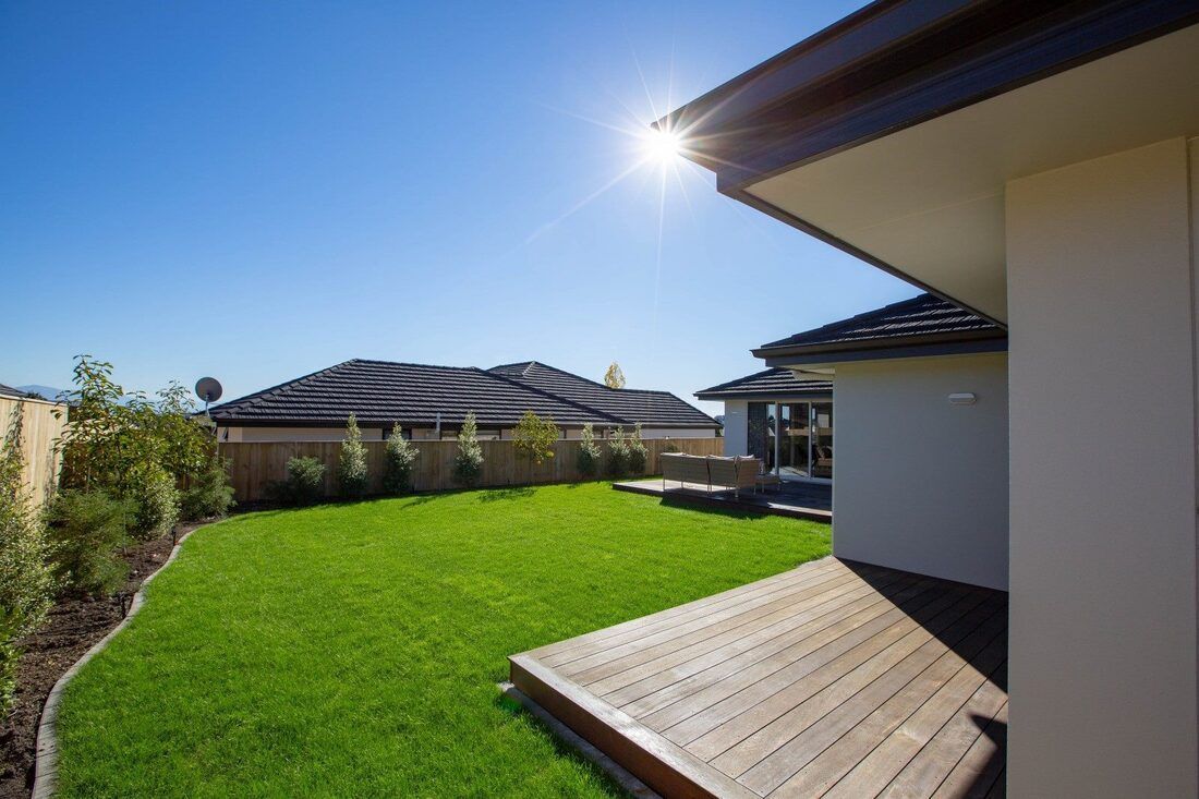 A house with a large lawn and a wooden deck in front of it.