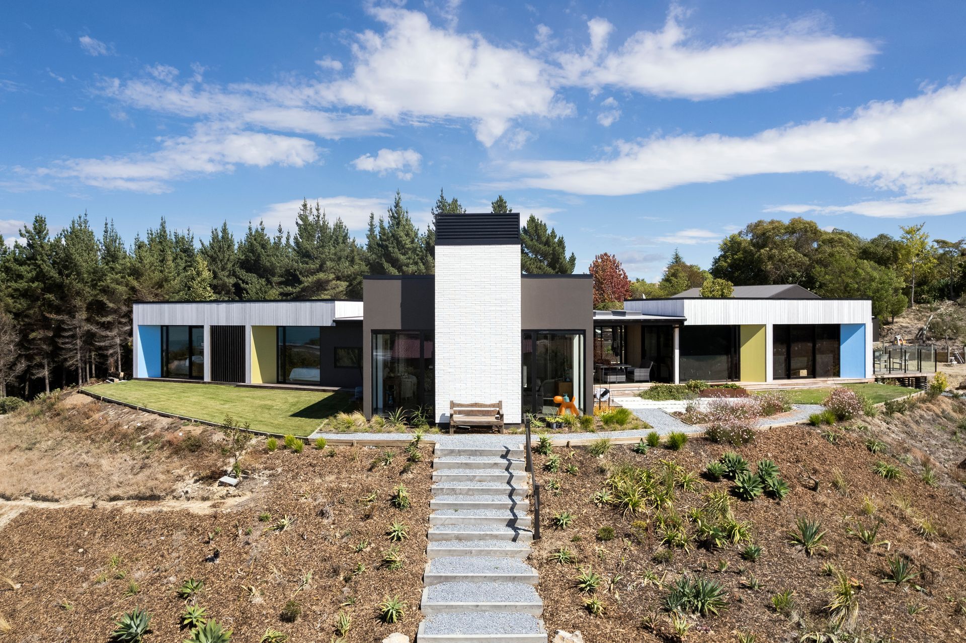 A modern house with stairs leading up to it is sitting on top of a hill surrounded by trees.