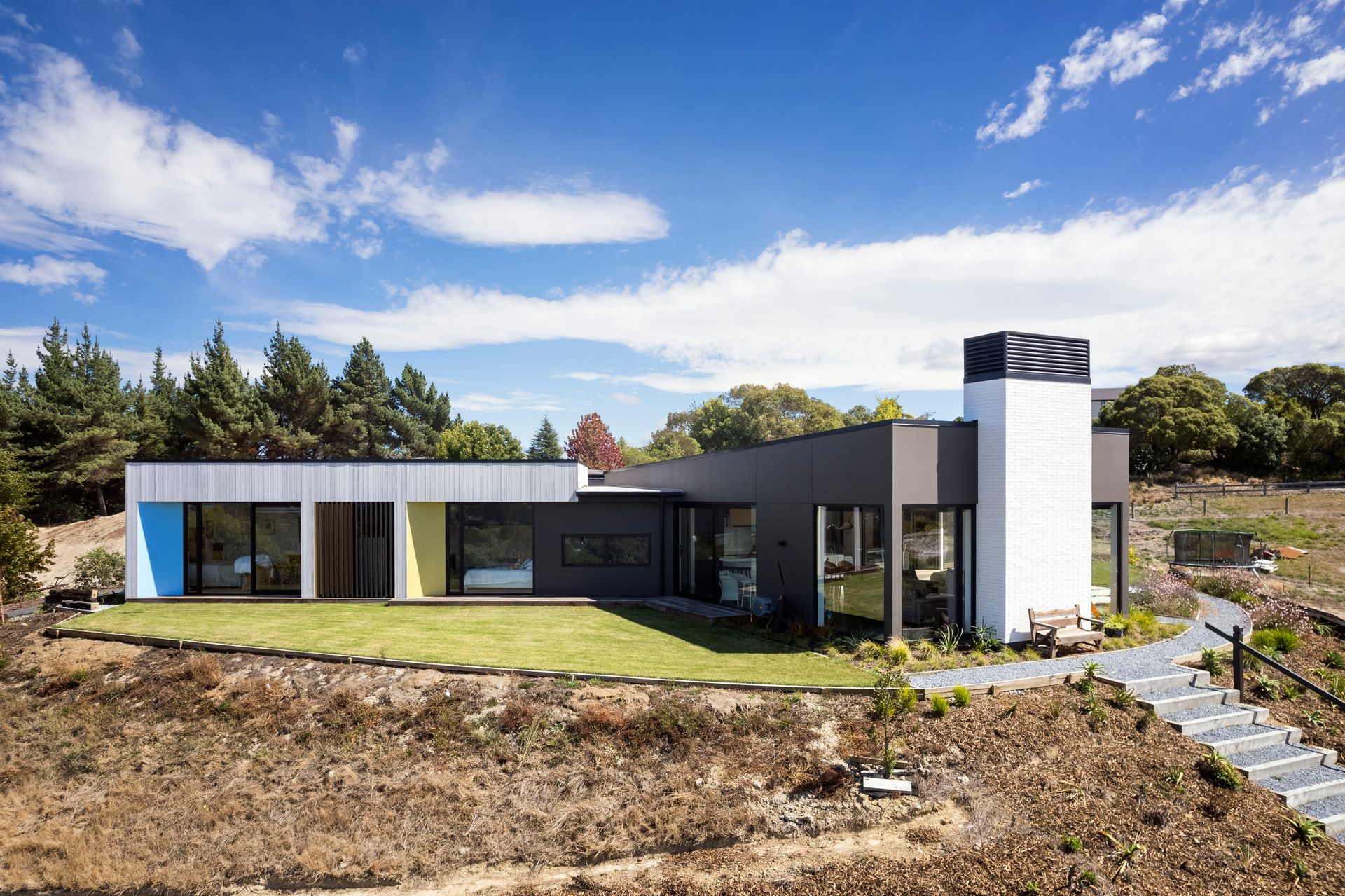 A modern house is sitting on top of a hill in the middle of a field.