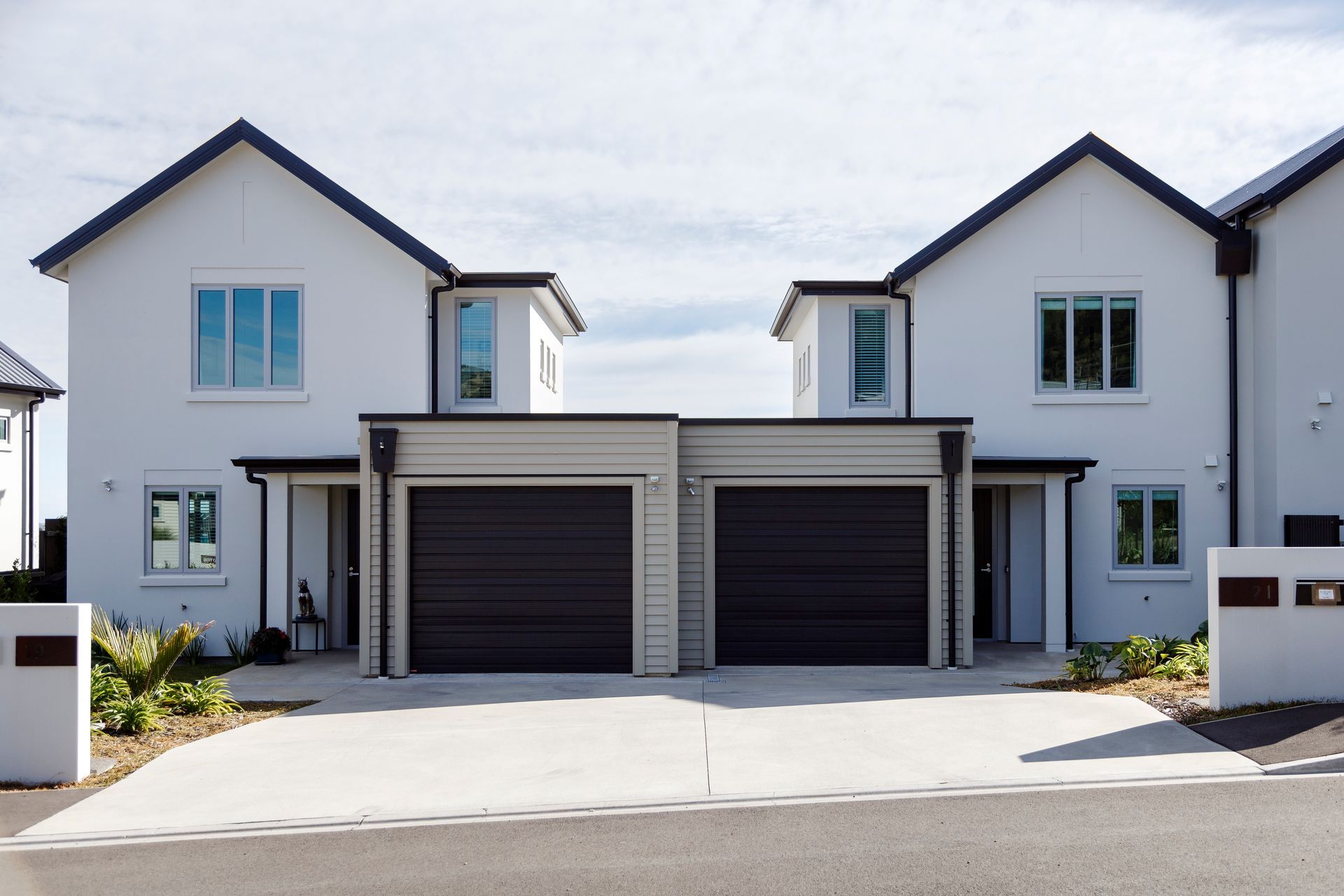 Two white houses with black garage doors are next to each other