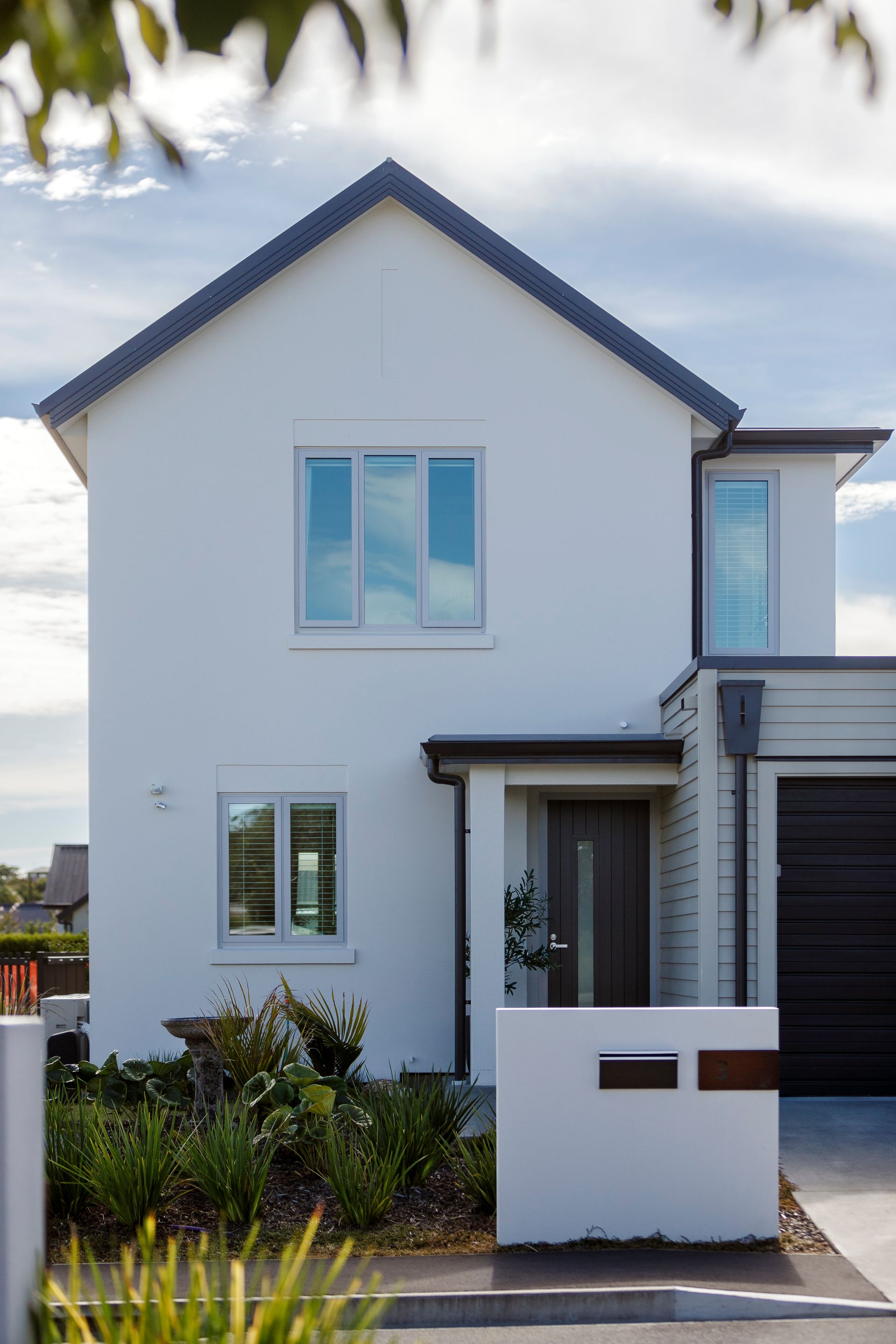 A white house with a black roof and a black garage door.