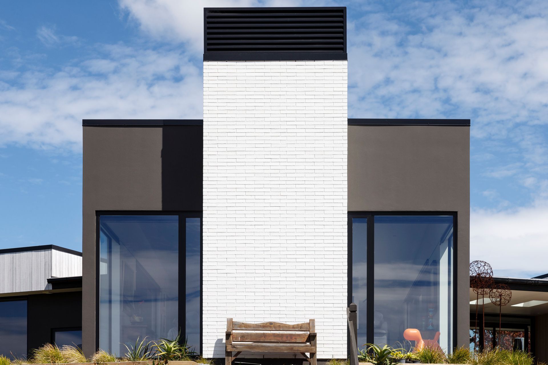 A modern house with a white chimney and a bench in front of it.