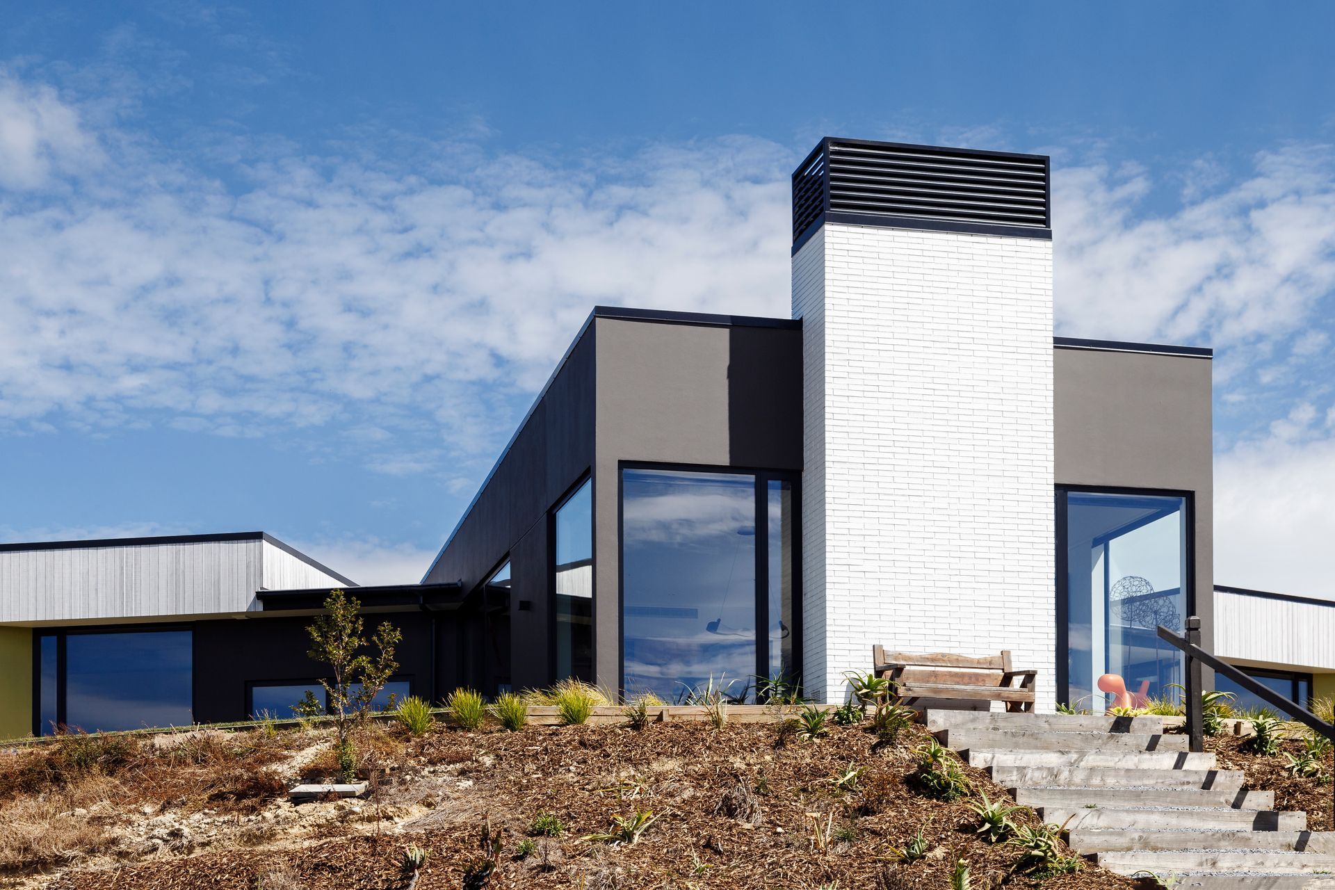 A modern house is sitting on top of a hill with stairs leading up to it.