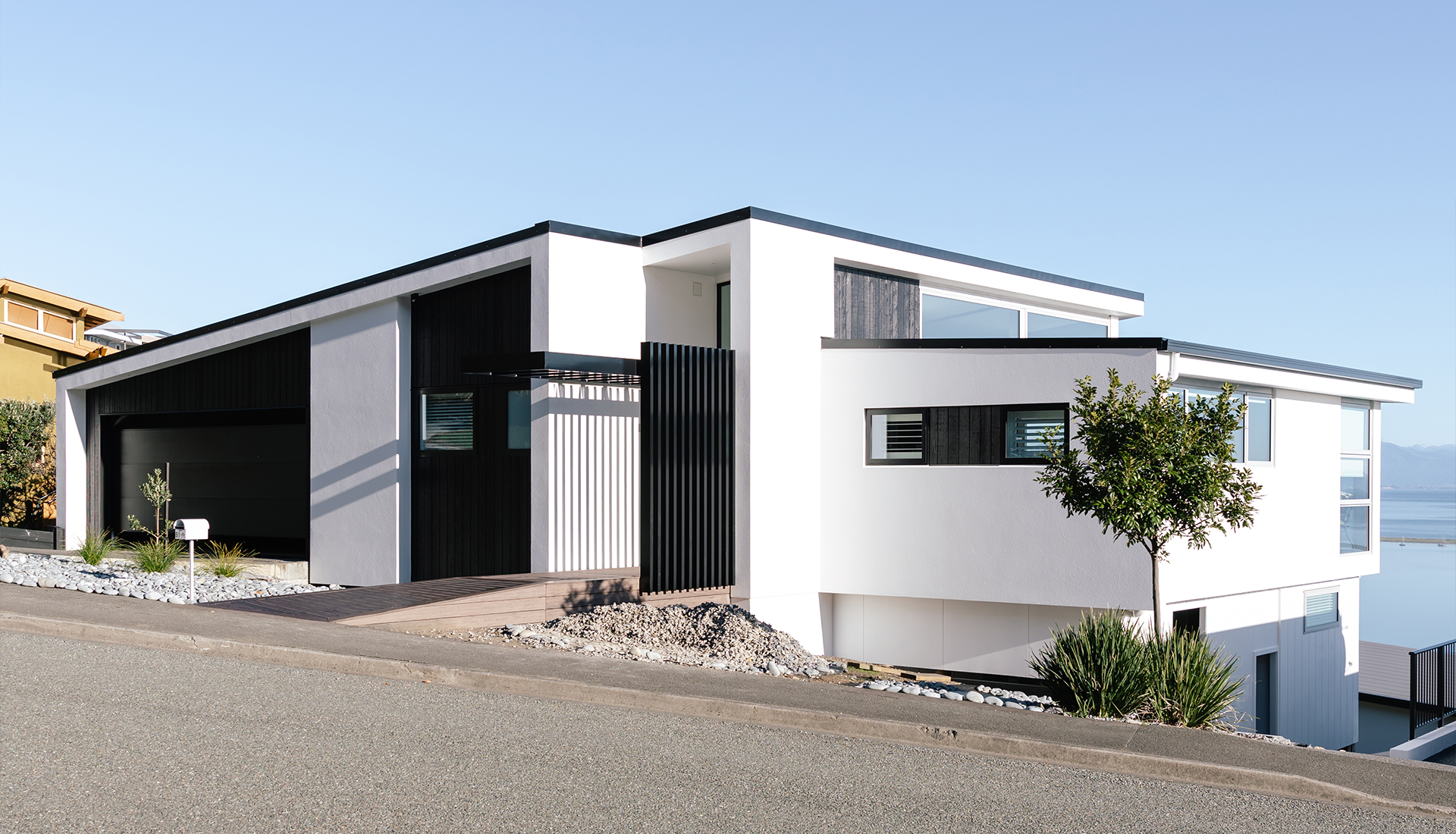 A white house with black trim sits on a hill overlooking the ocean