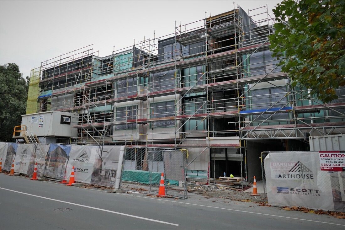 A large building under construction with scaffolding and cones on the side of the road.