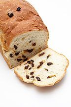 A loaf of raisin bread with a slice taken out of it on a white background.