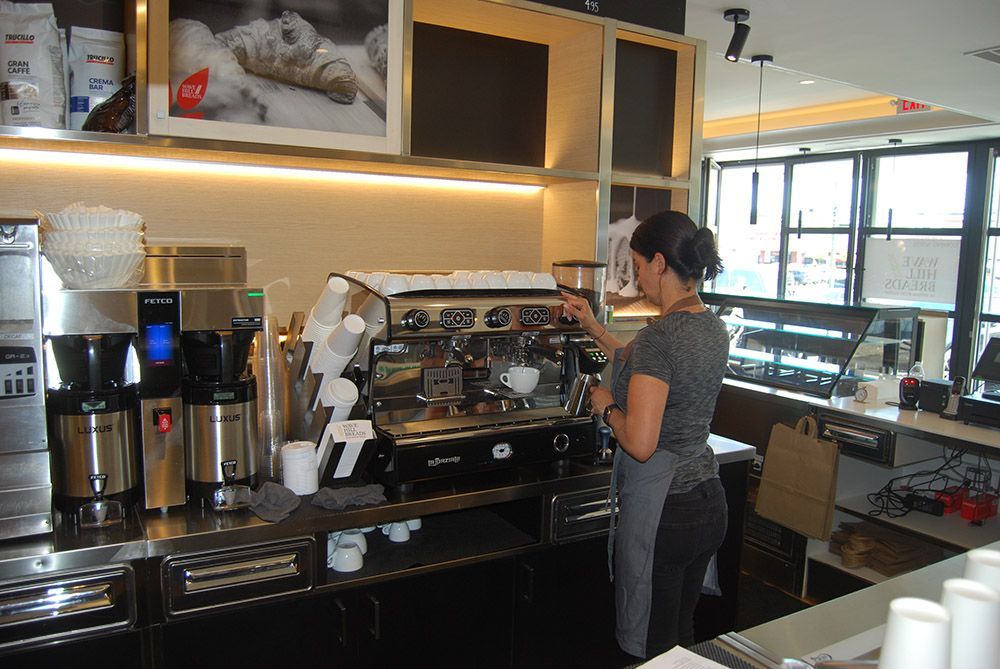 A woman in a gray shirt is making a cup of coffee