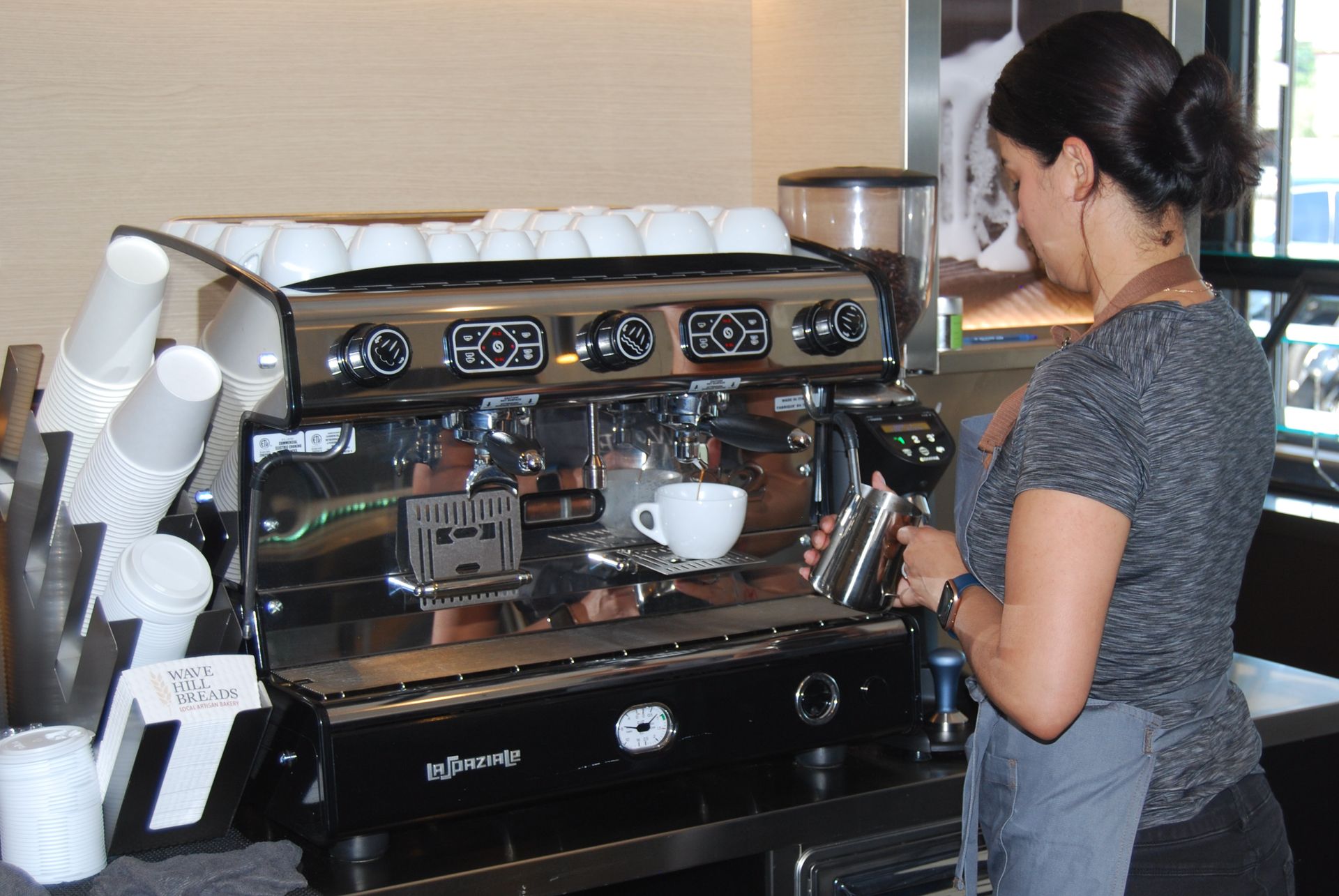 A woman prepares a cup of coffee in front of a machine that says ' wheel ' on it