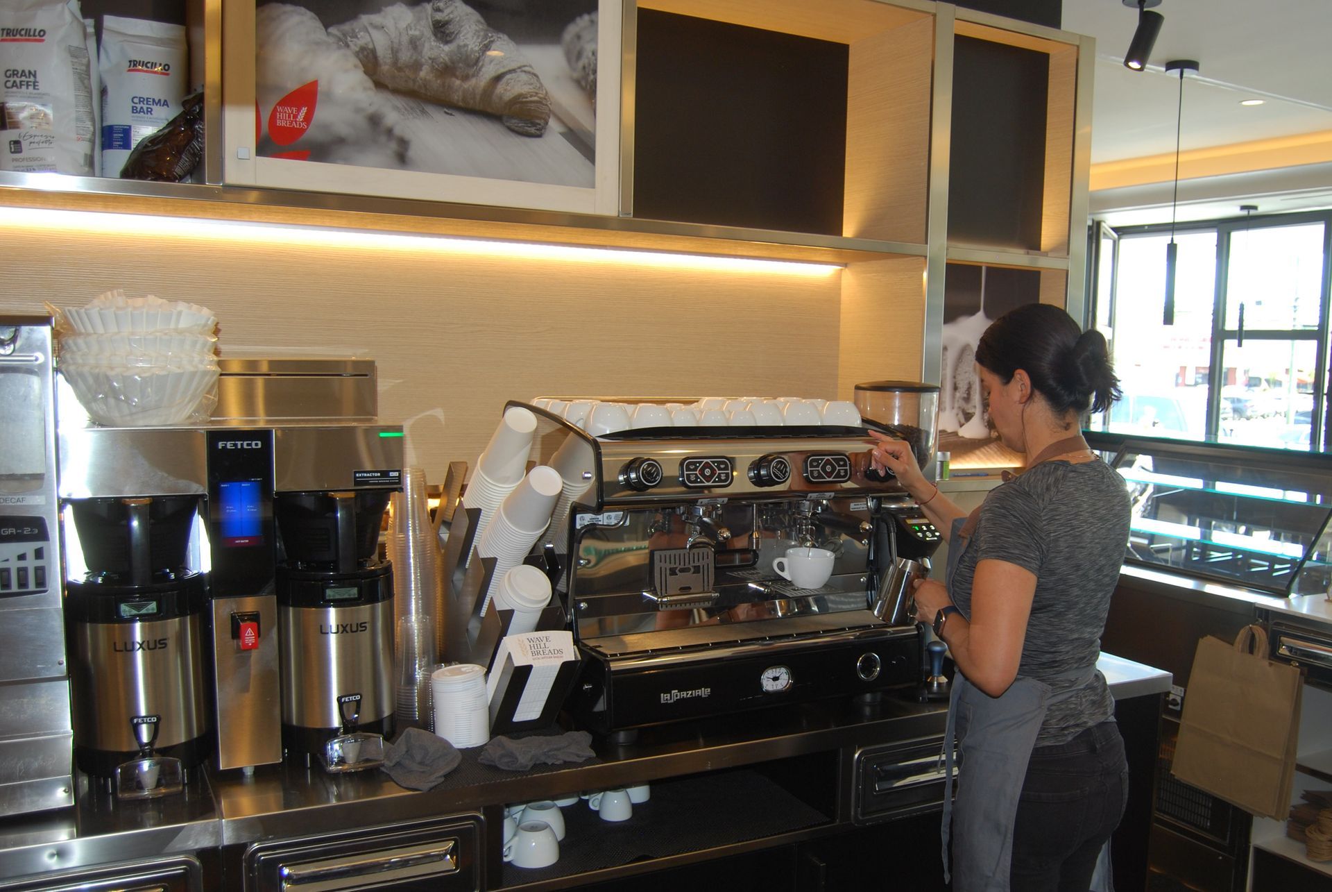 A woman stands in front of a coffee machine with a sign above it that says 2x