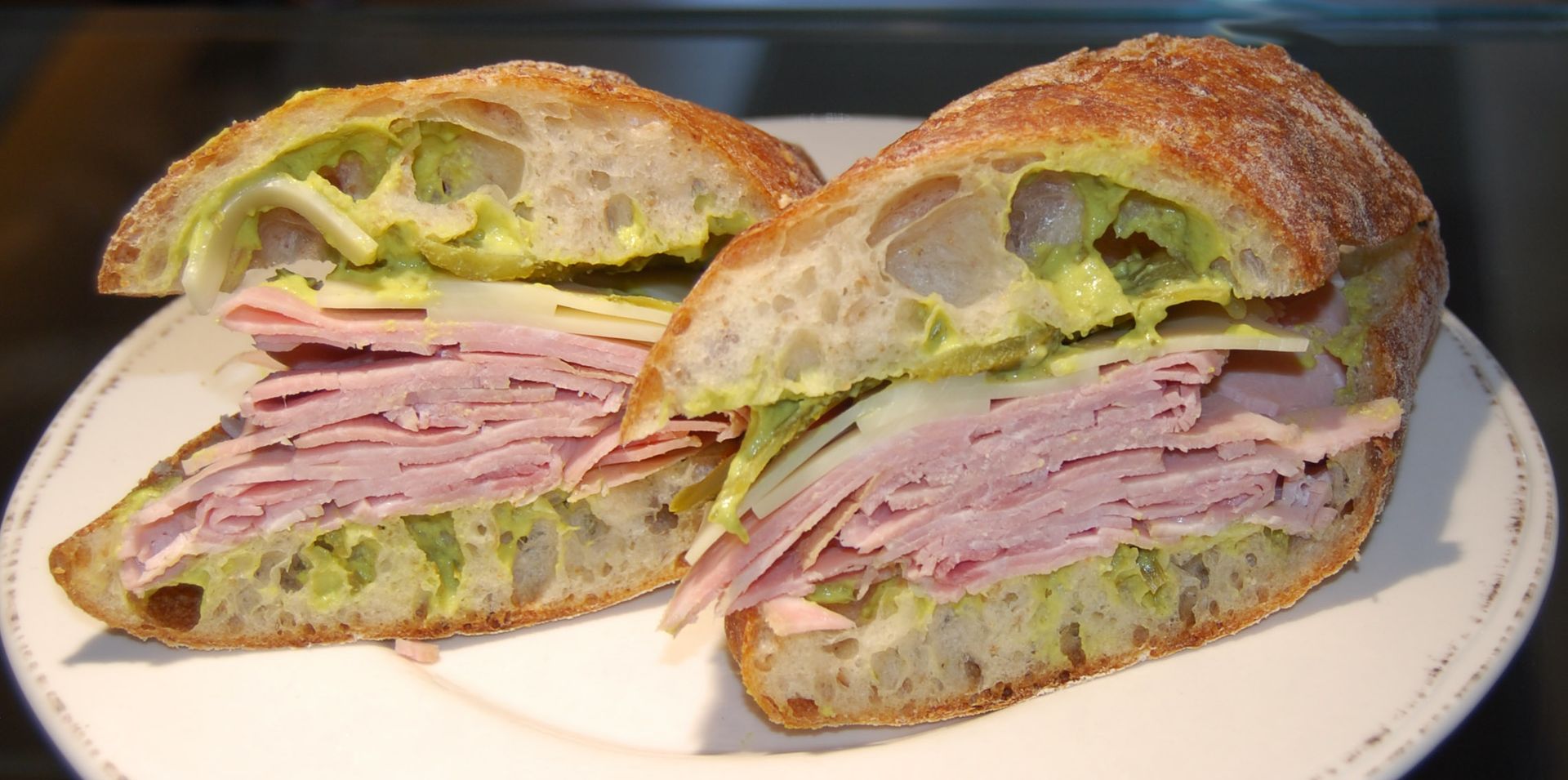 Two halves of a ham and avocado sandwich on a white plate