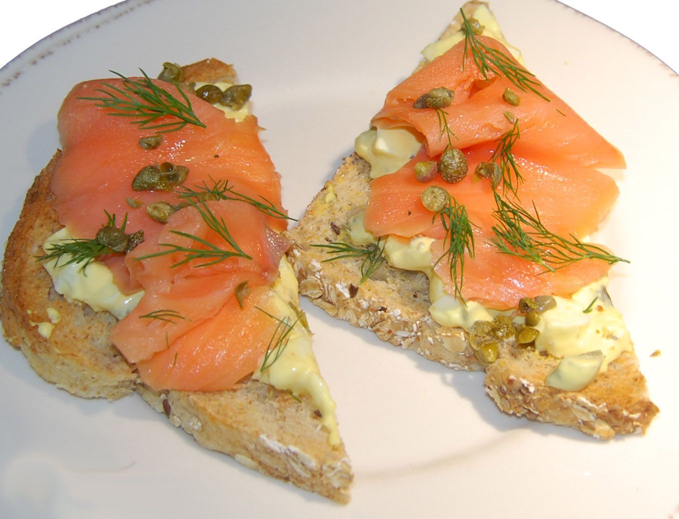 Two slices of toast with salmon and capers on them on a white plate