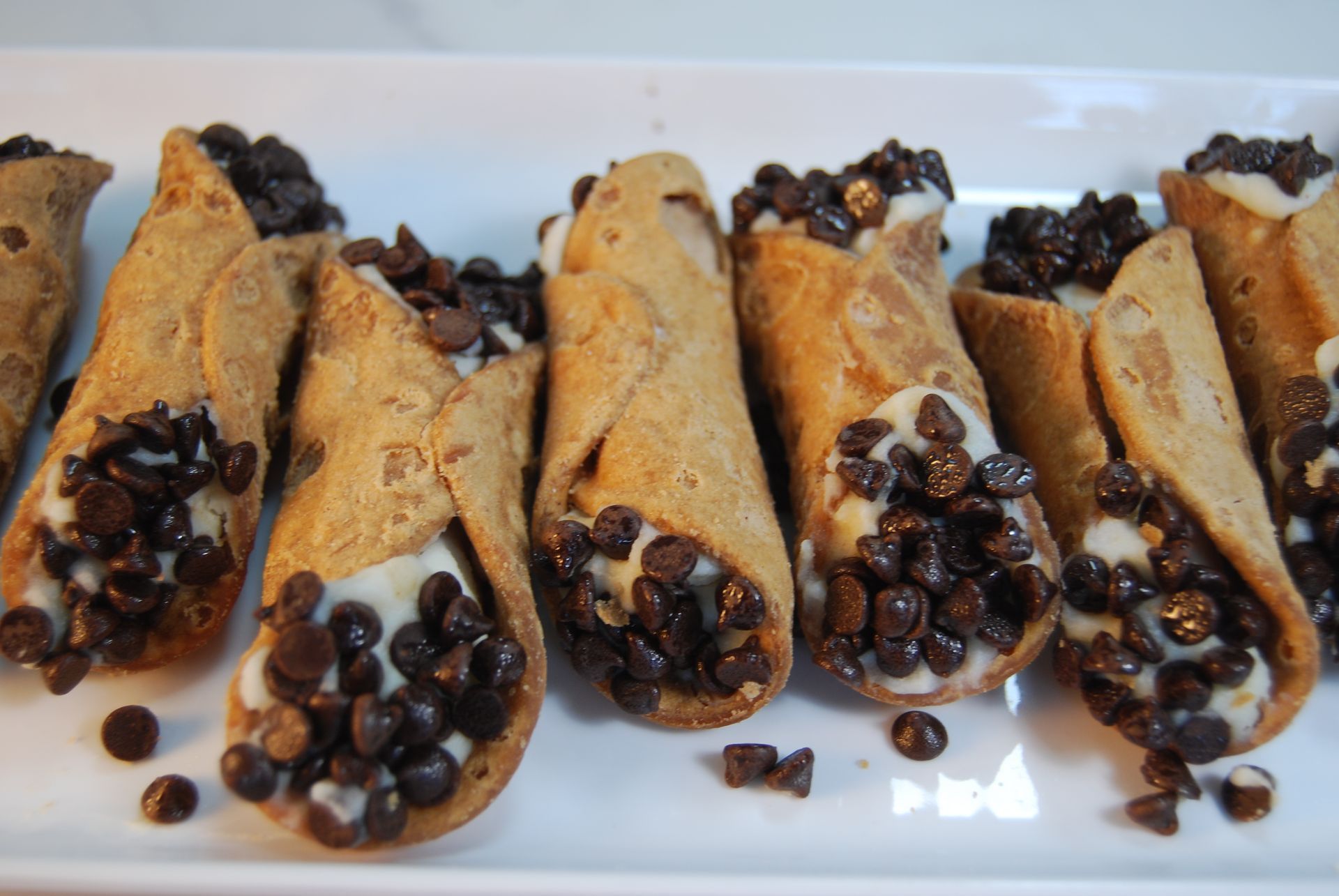 A row of cannoli with chocolate chips on a white plate