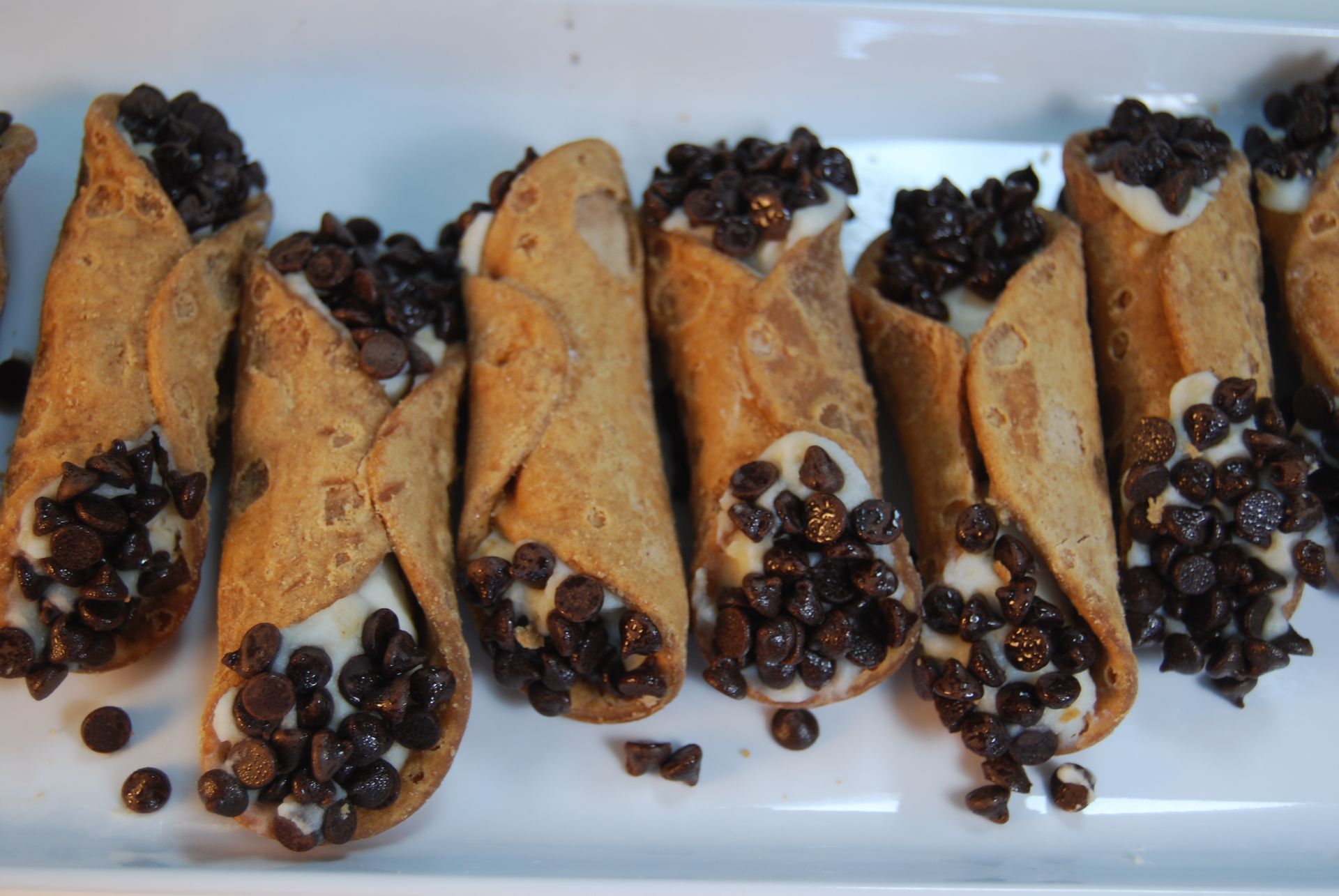 A row of cannoli filled with chocolate chips on a white plate