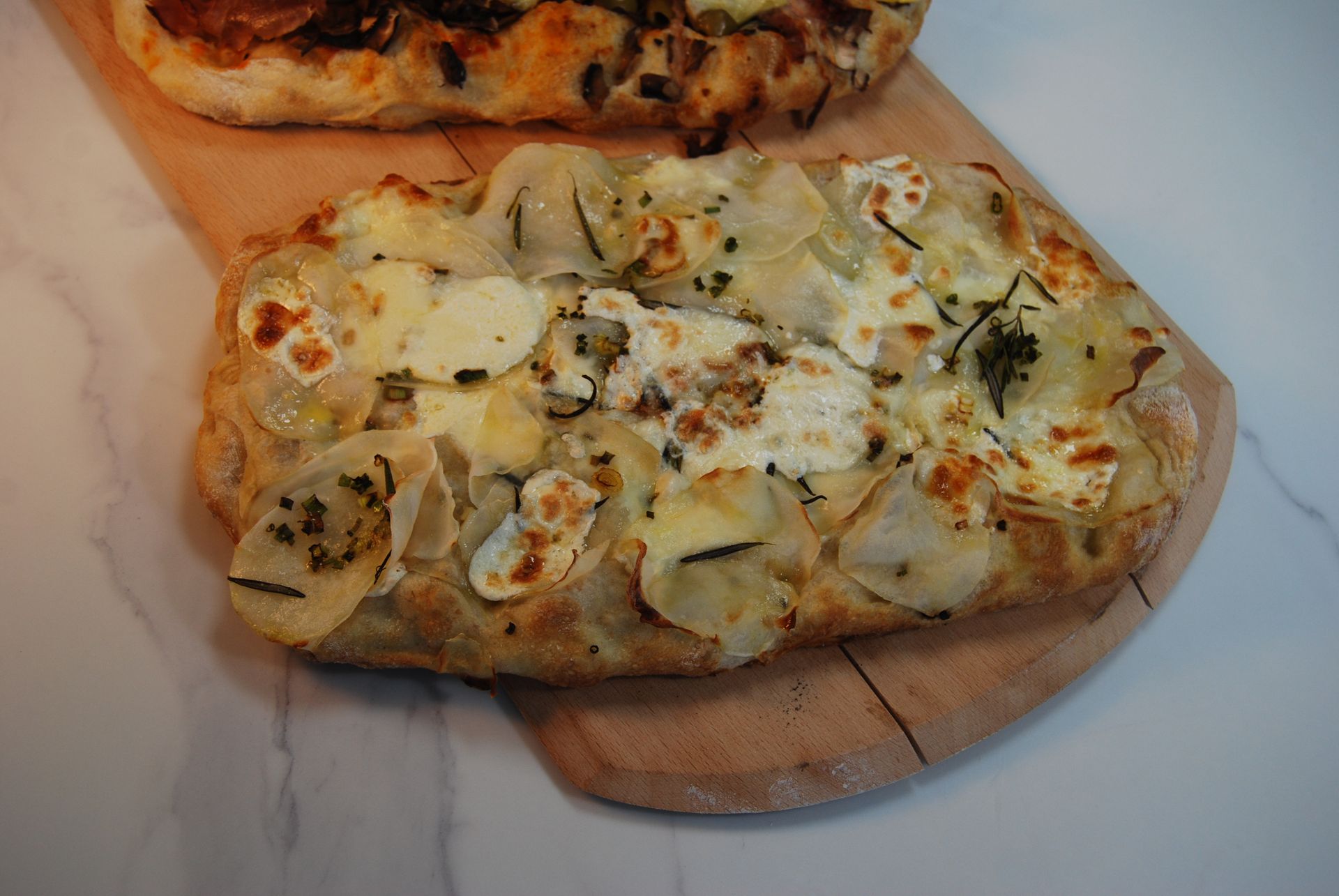 A pizza with potatoes and cheese is on a wooden cutting board