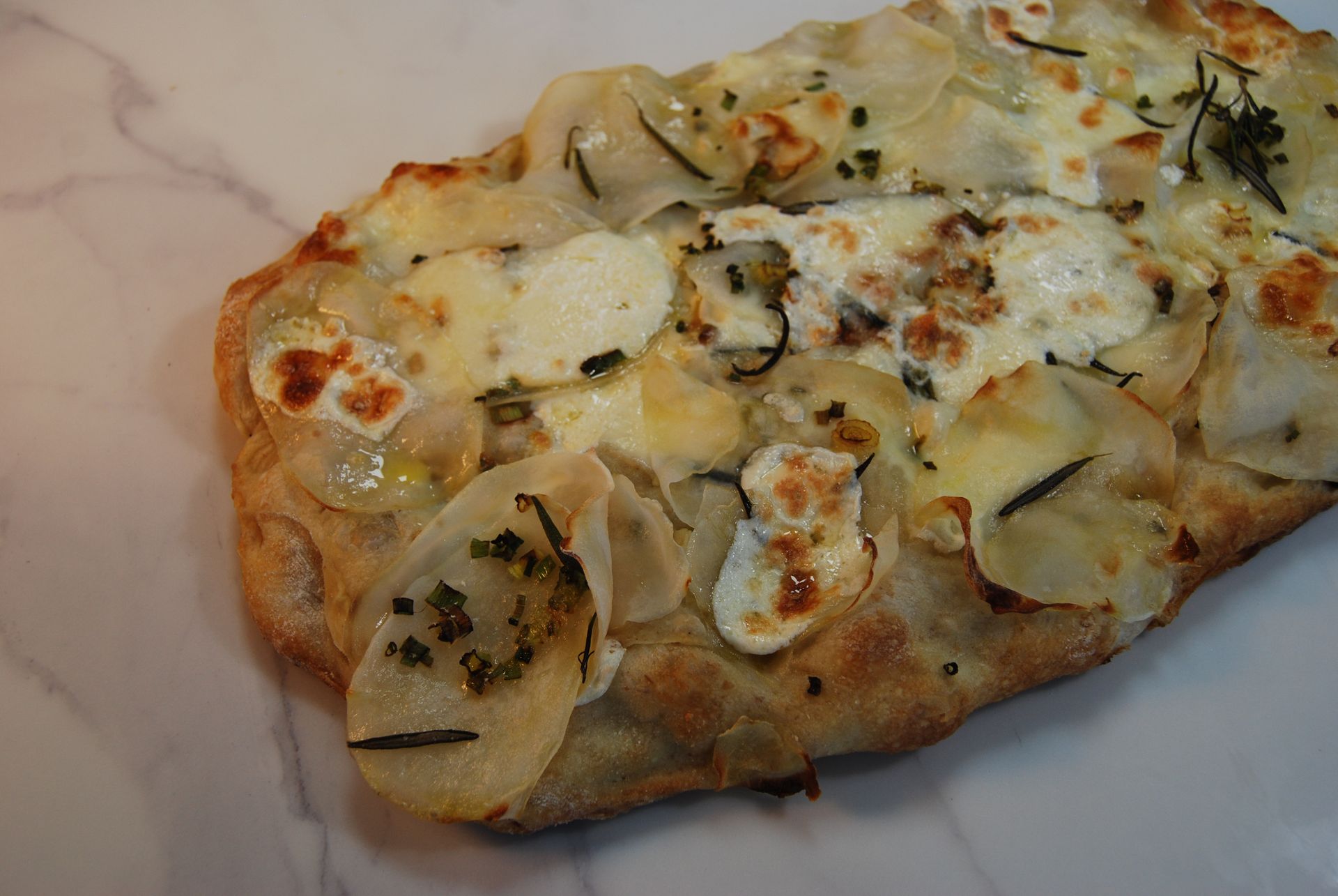 A close up of a pizza with potatoes and cheese