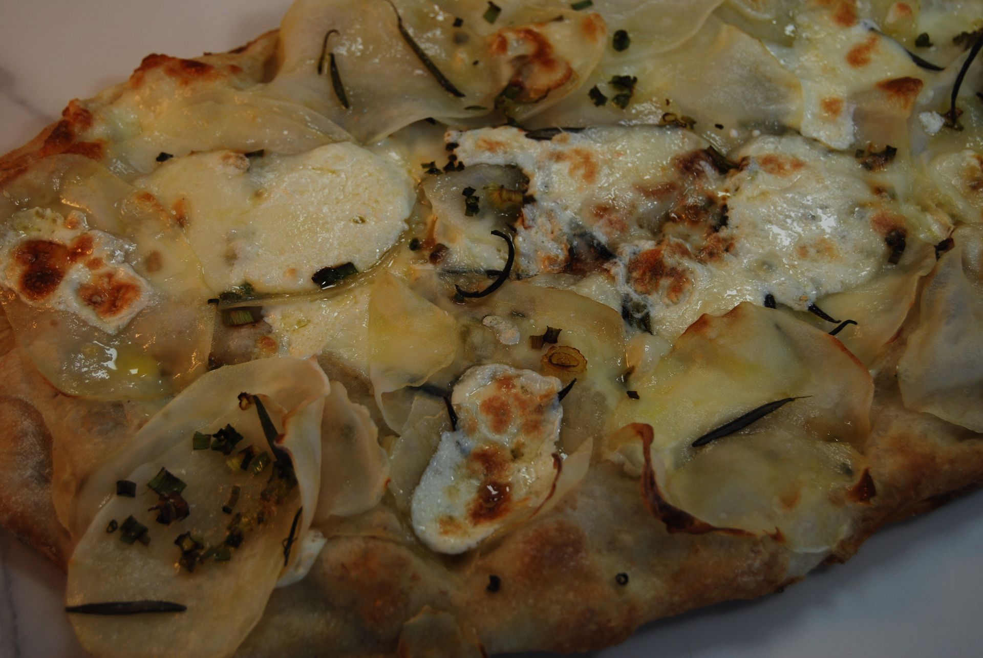 A close up of a pizza with potatoes and cheese