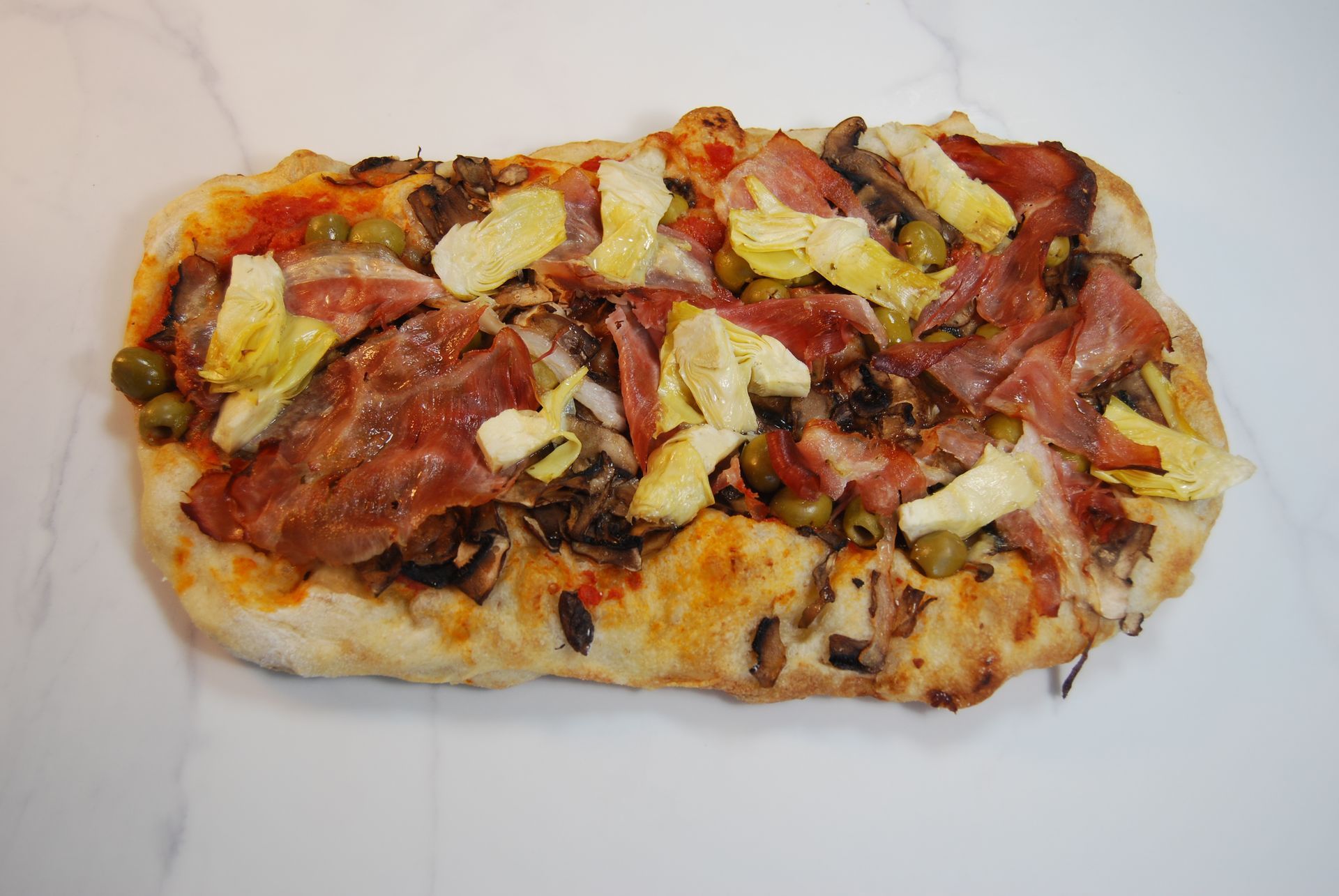 A pizza with bacon artichokes and olives on it