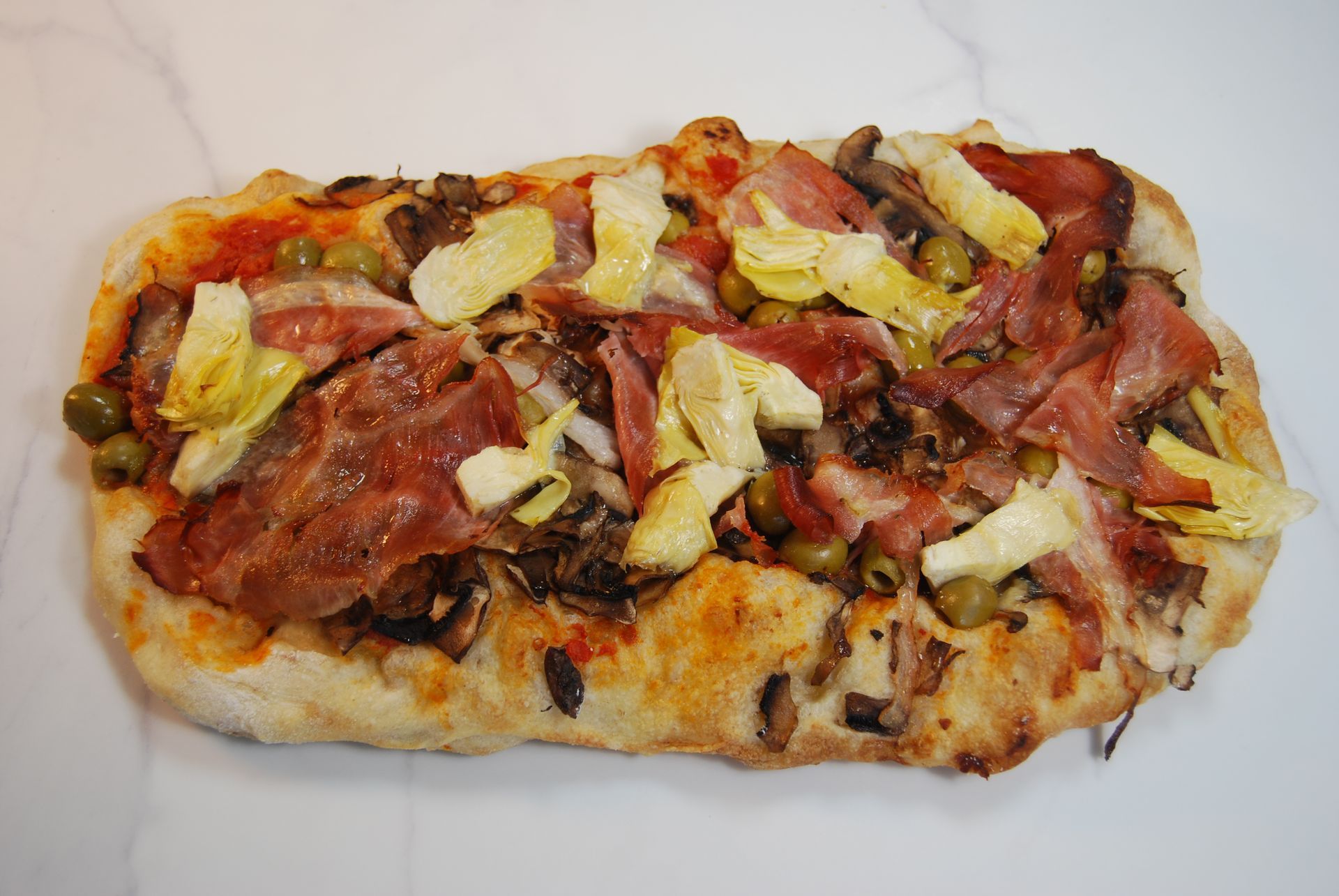 A pizza with bacon artichokes and olives on it