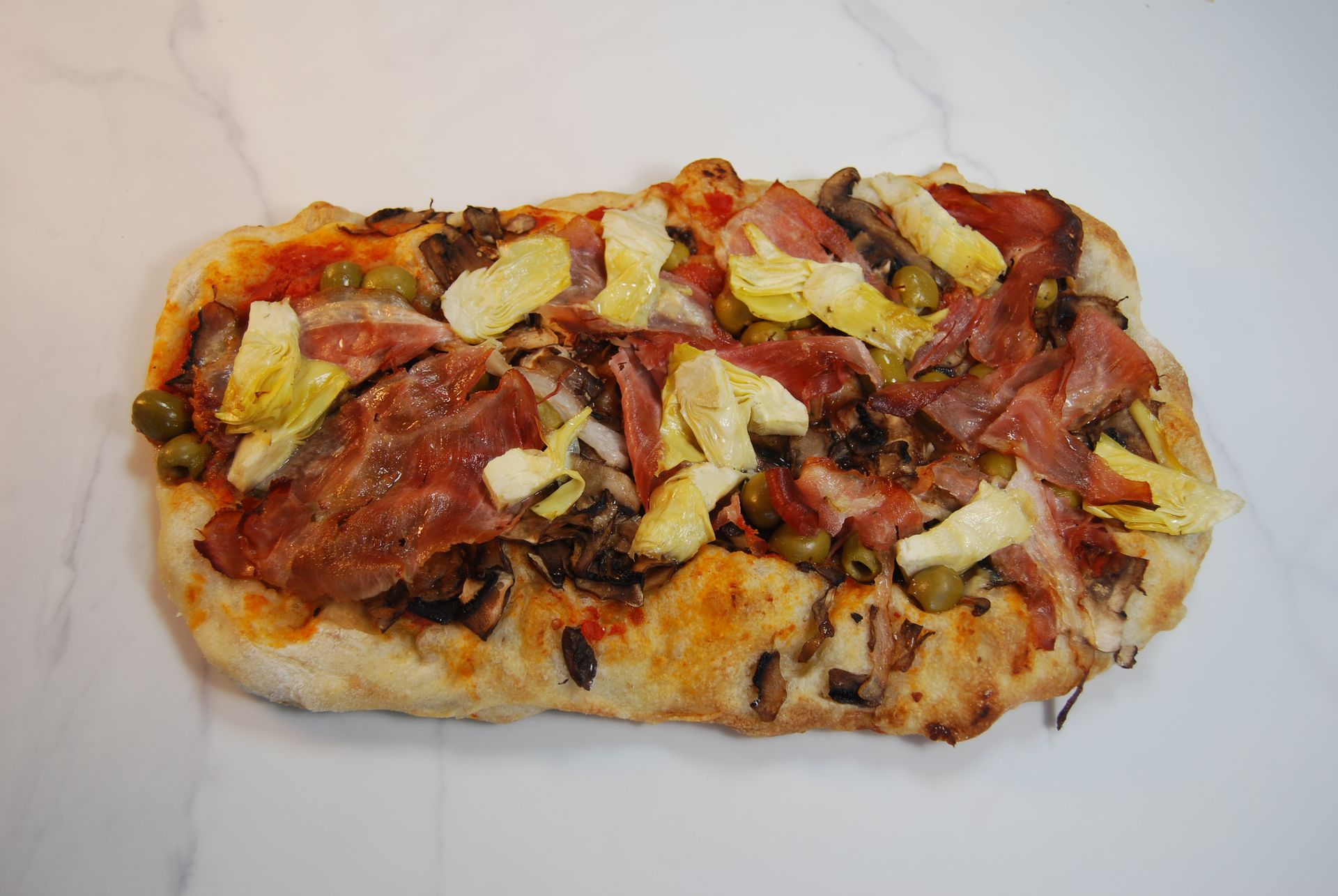 A pizza with bacon artichokes and olives on it