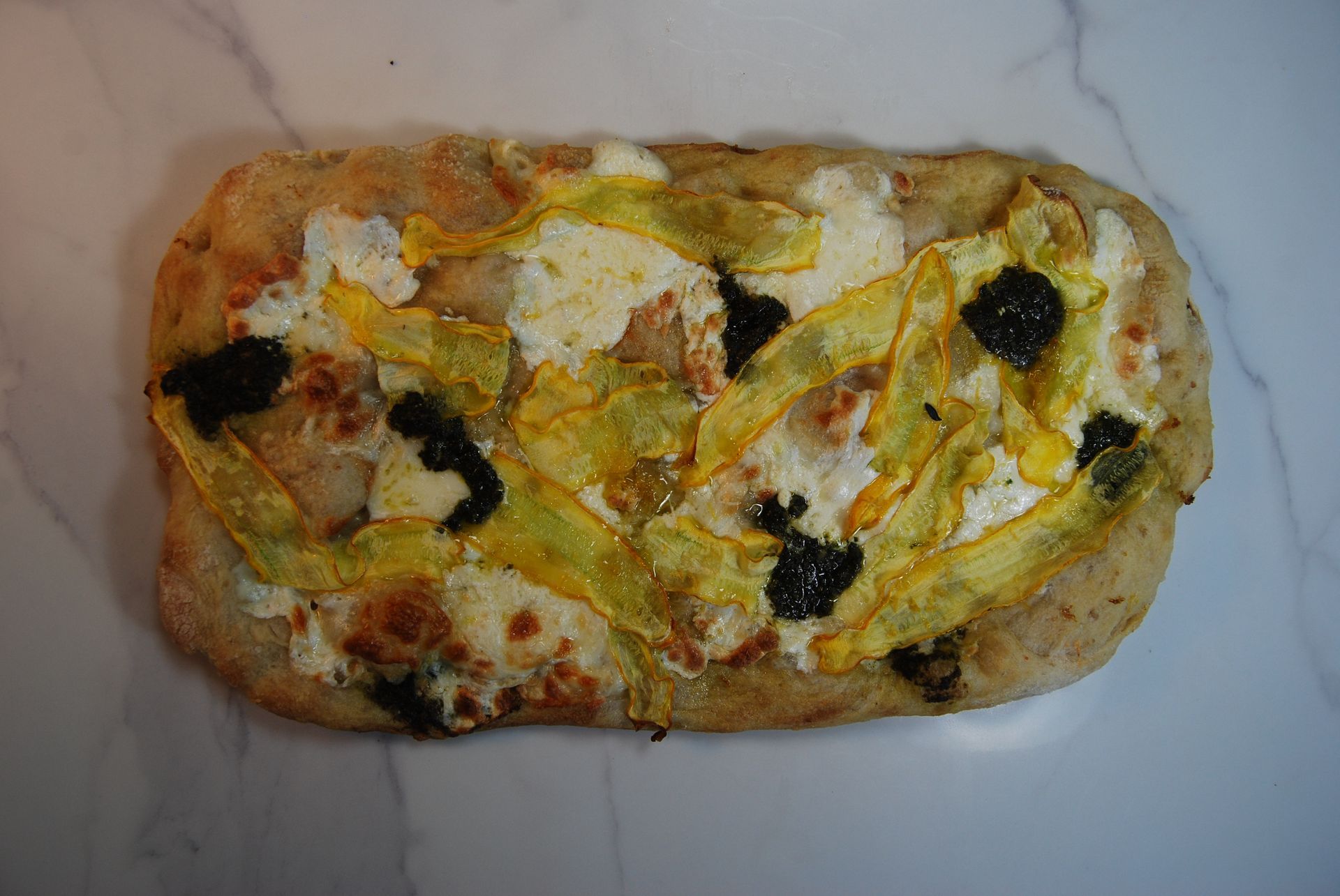 A pizza with yellow peppers and black olives on it