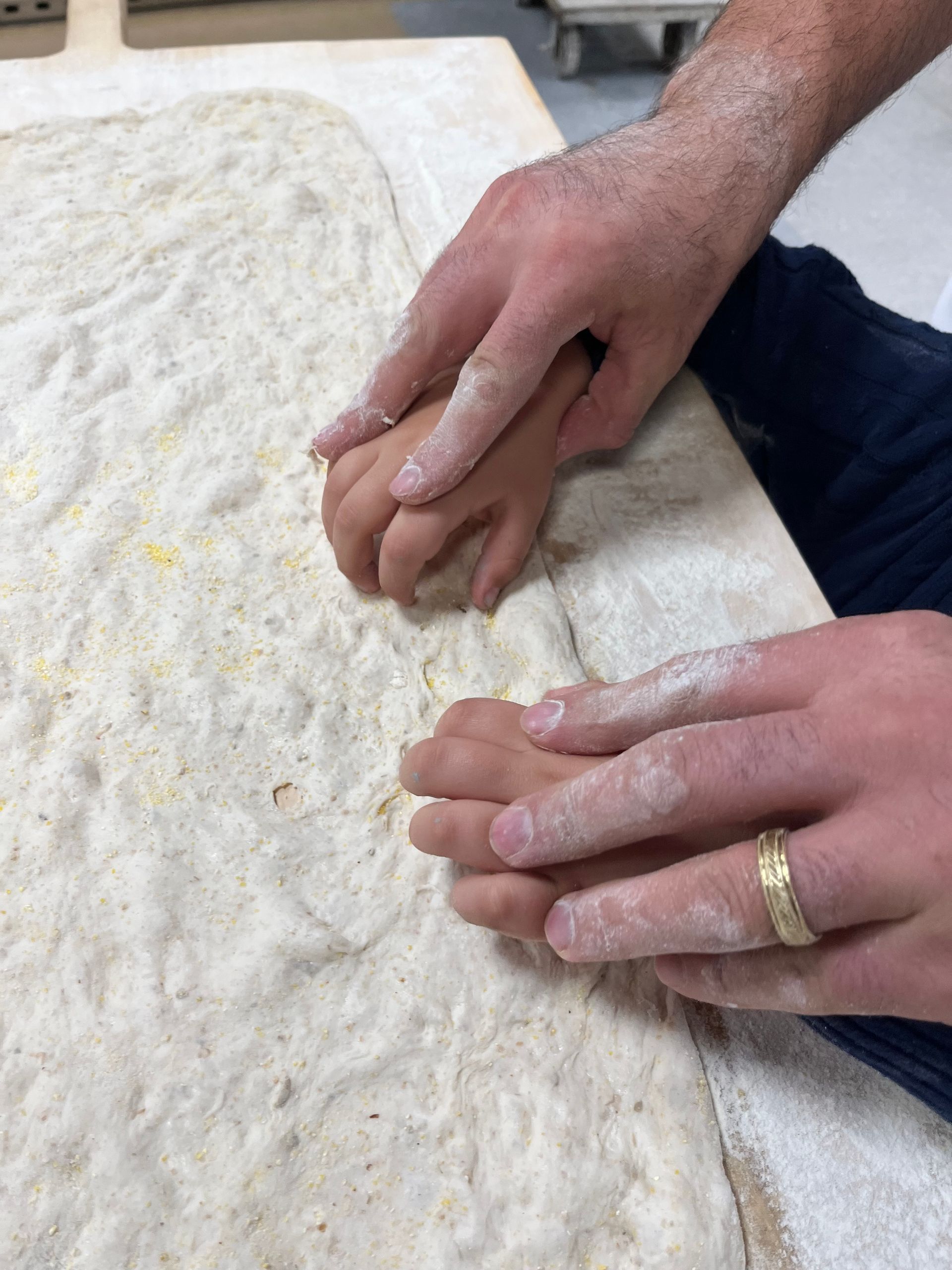 A man and a child are holding hands over a piece of dough