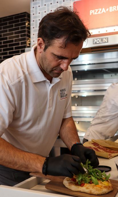 A man prepares a pizza in front of a sign that says pizza