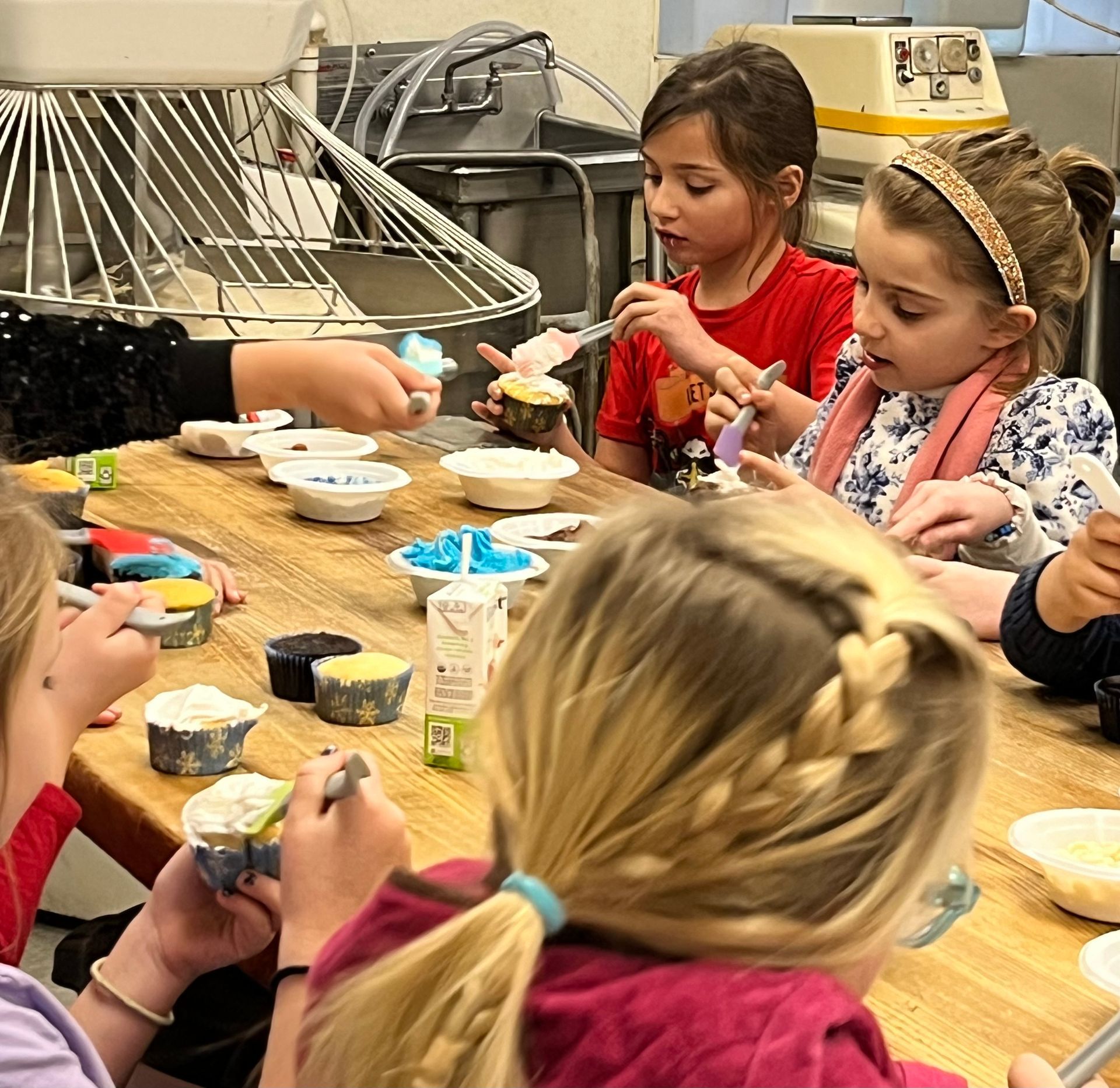 A group of young girls are sitting at a table decorating cupcakes