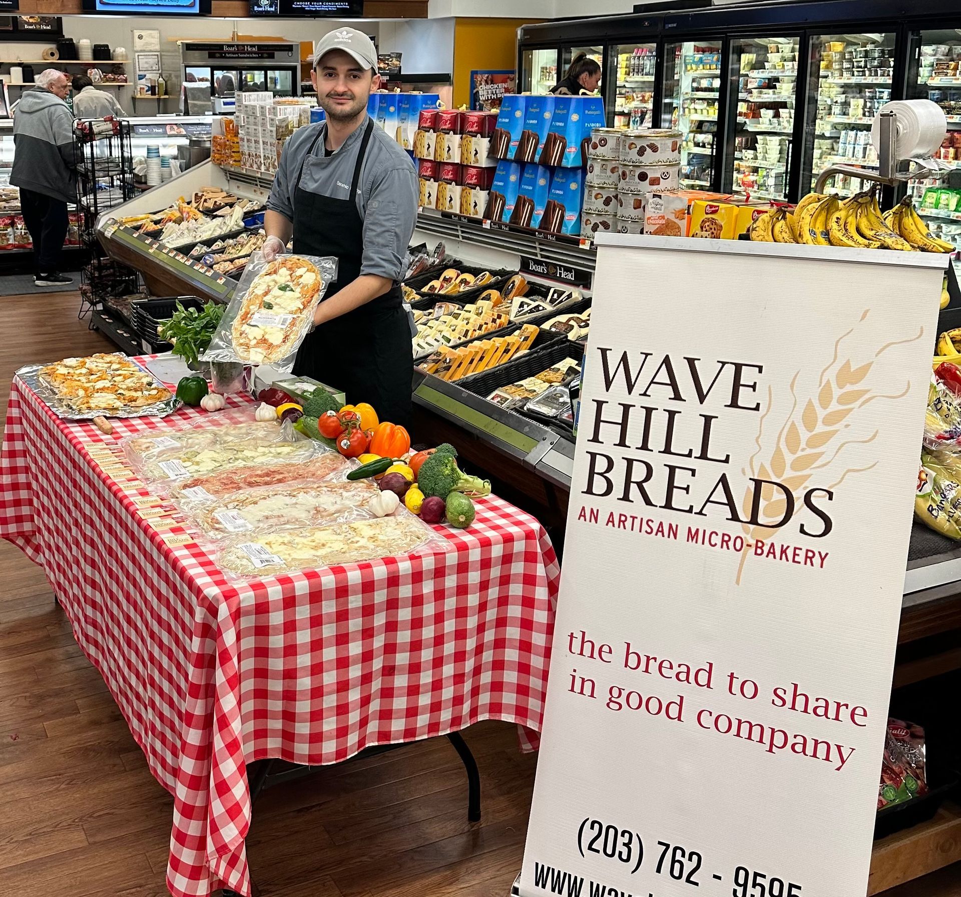 A man holding a pizza in front of a table that says wave hill breads