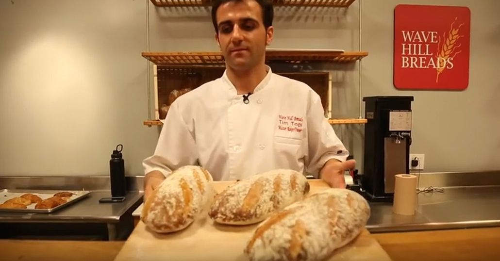 Master Baker Tim Topi is holding three loaves of bread on a wooden cutting board.