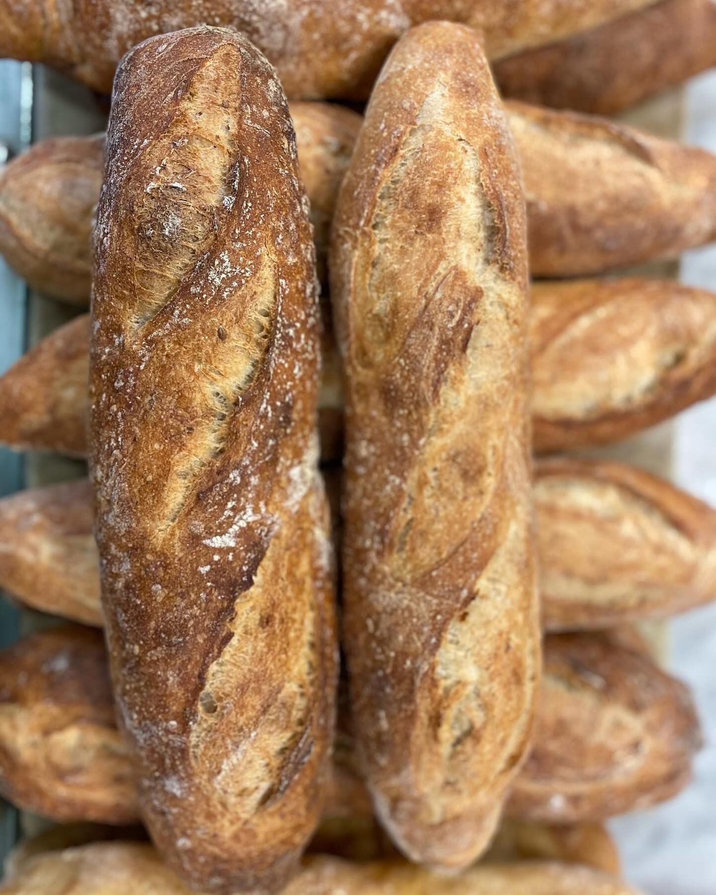 A bunch of loaves of bread are stacked on top of each other on a table.