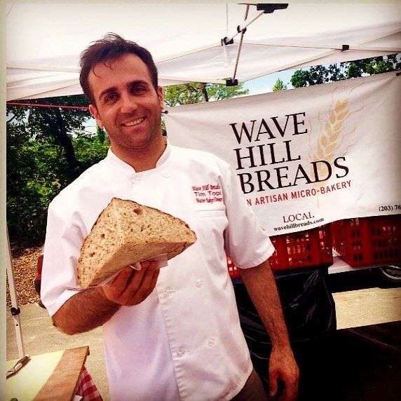 A man holding a loaf of bread in front of a wave hill breads sign