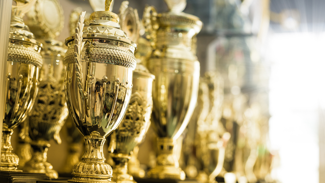 A row of gold trophies sitting on top of each other on a shelf.