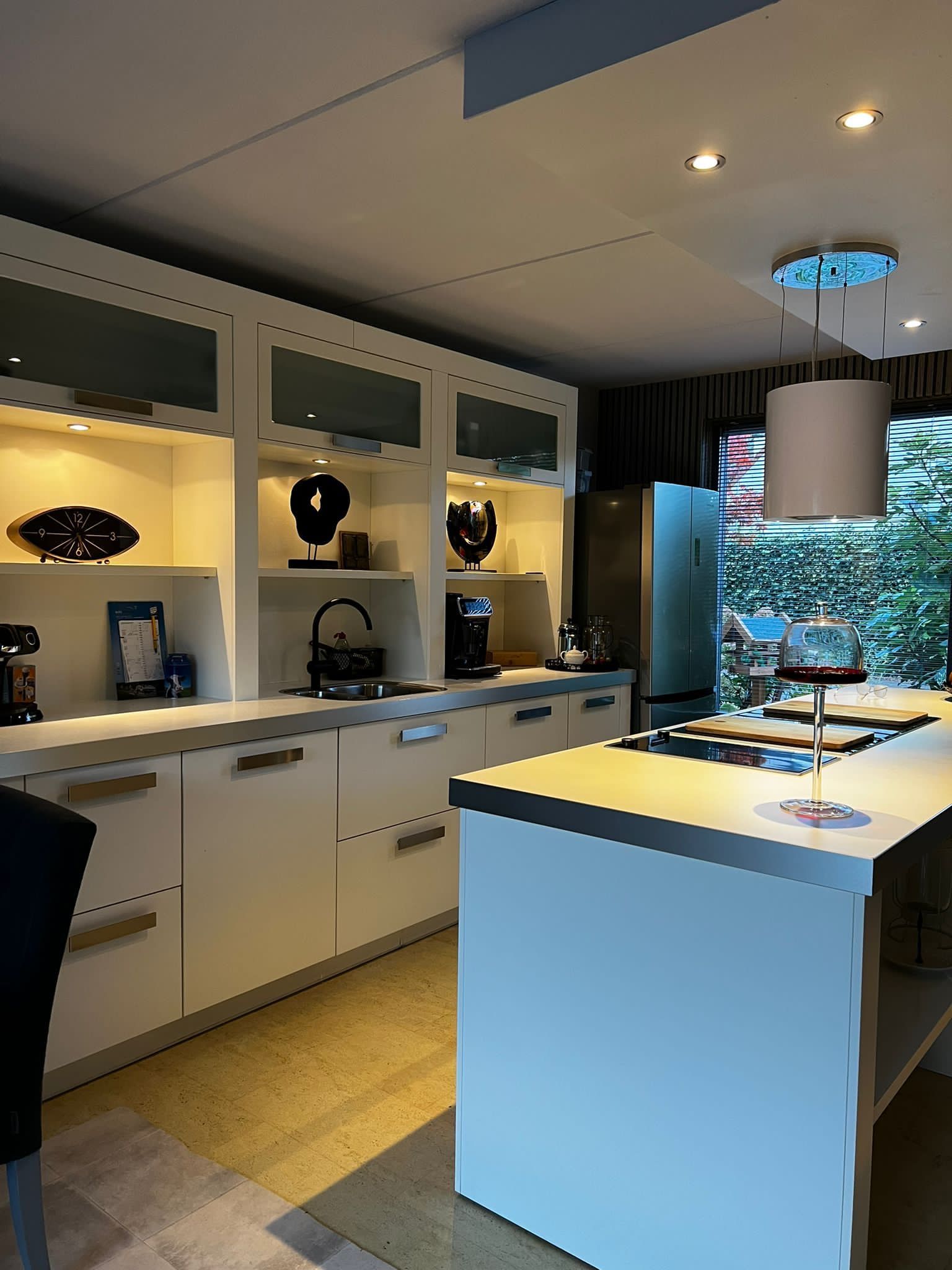 Witte keuken met kookeiland, kasten en apparatuur. Warme verlichting accentueert decoraties en aanrechtbladen.