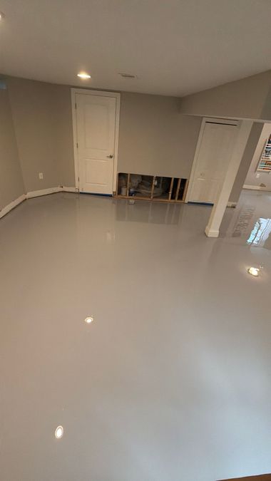 Empty beige room with glossy gray floor, white doors, and a small stack of chairs in the back.