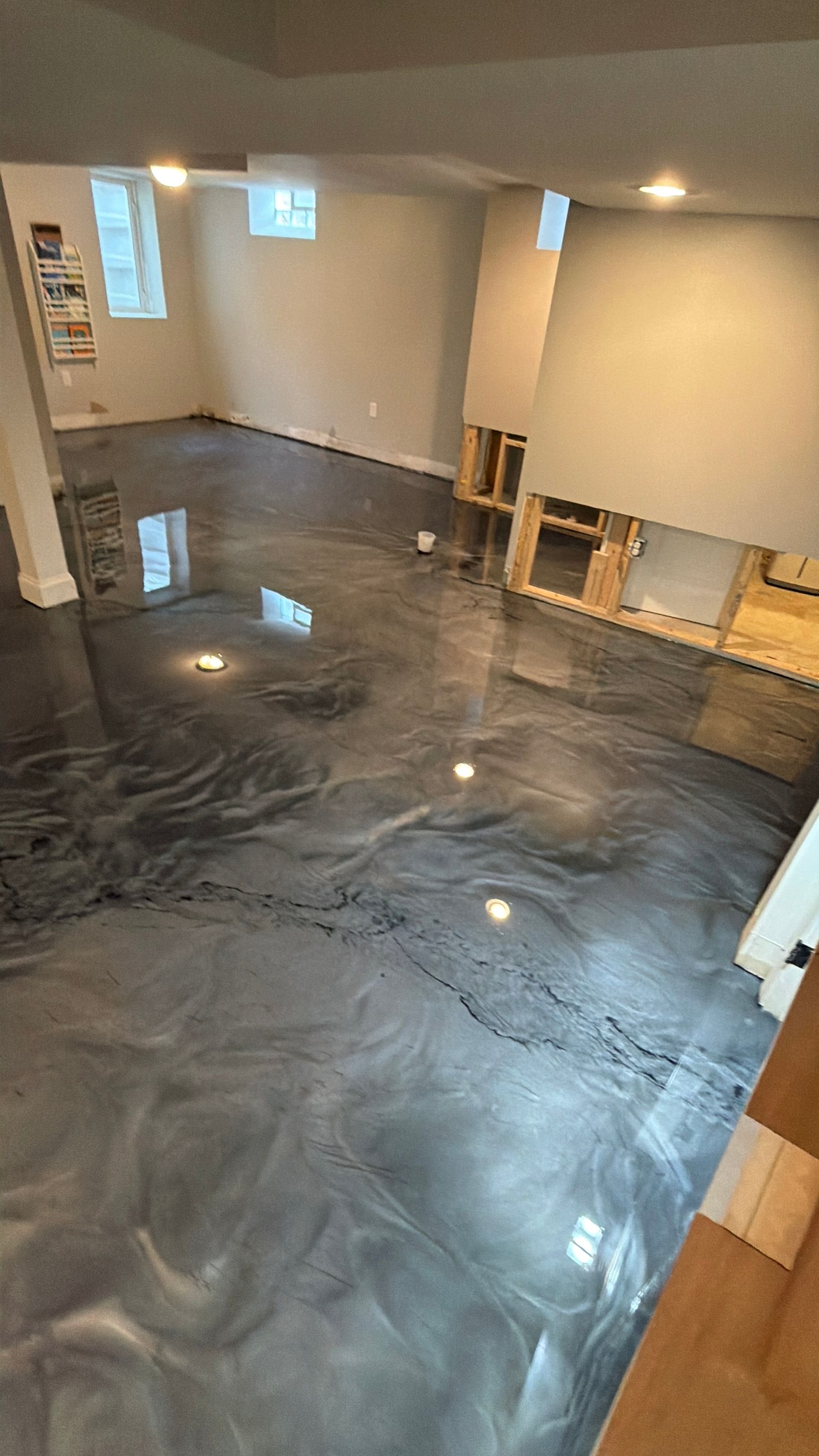 Empty room with glossy black epoxy floor and exposed wall framing under renovation