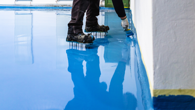 Worker boots walking across a glossy blue epoxy floor in a room under construction