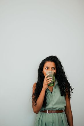 A woman in a green dress is drinking a green smoothie.