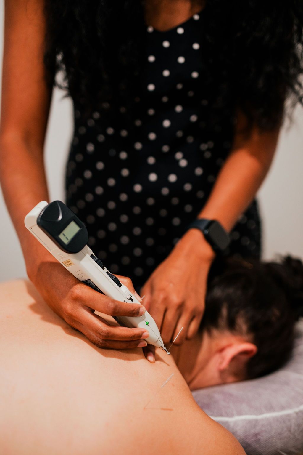 A woman is giving a woman a electro acupuncture treatment on her back.