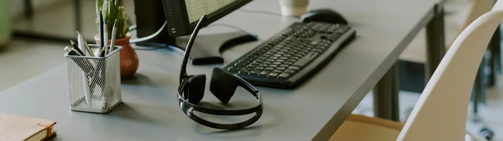 Office desk with keyboard, glasses, and a pen holder. A white chair is in the background.